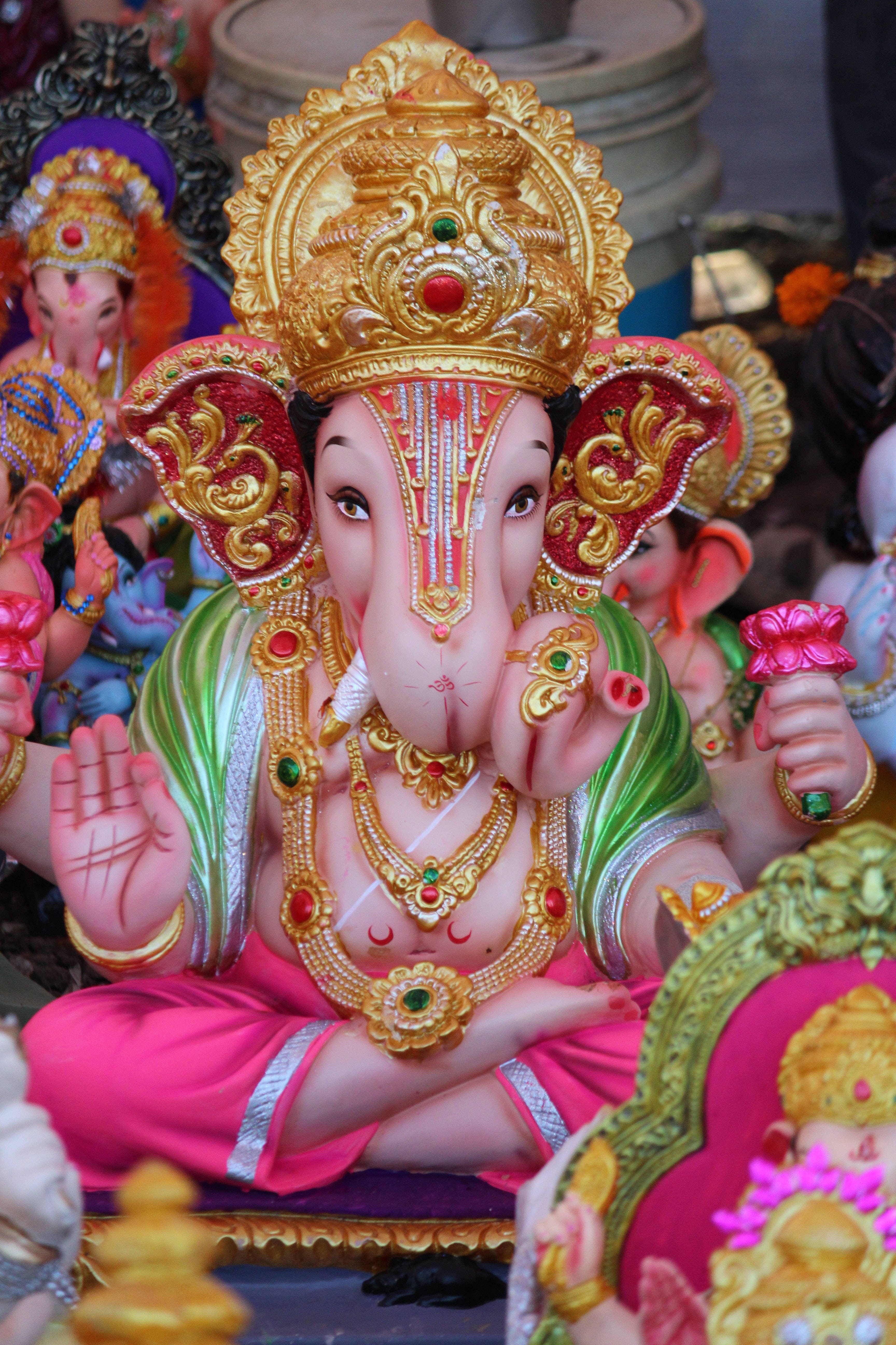 ganesh iPhone 桌布 壁紙 — 一尊色彩鮮豔的黃金象神甘尼許雕像，飾有珠寶和彩色服飾，在其他節日人偶中顯眼地坐著。