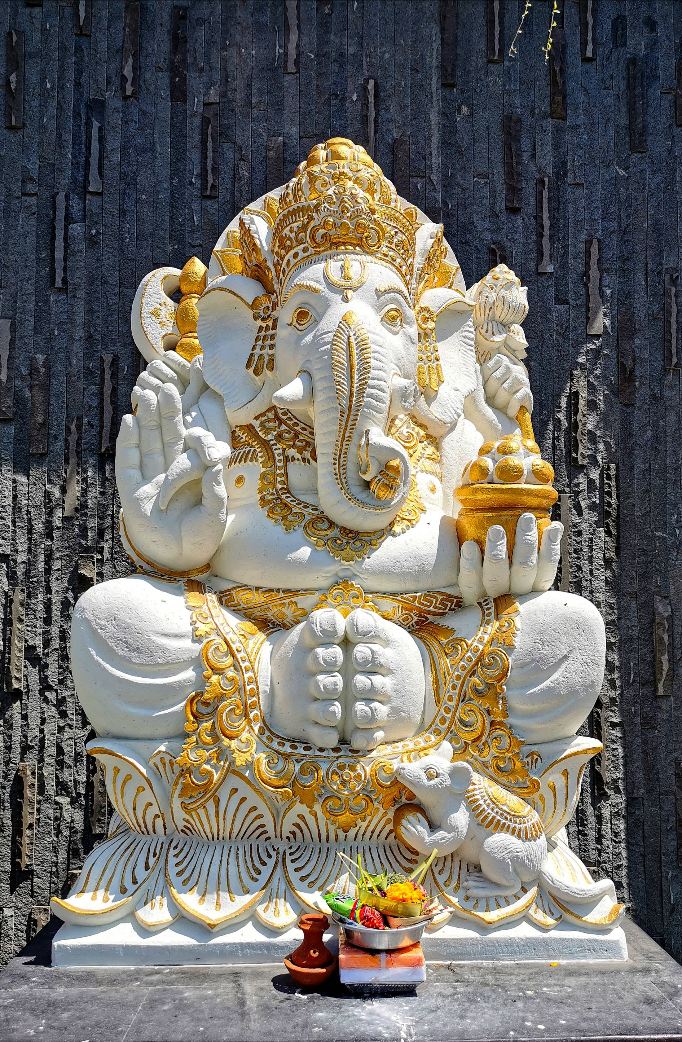 Ganesh 桌布 壁紙 — 一尊莊嚴的白金色象神雕像，靜靜地坐在深色木牆前，底座上放有供品。