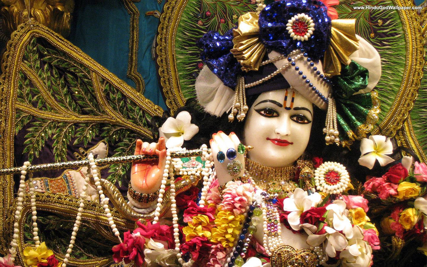 Hindu Temple 桌布 壁紙 — 一尊裝飾華麗的印度教神像，飾有精緻的珠寶花朵和鮮豔的藍金色皇冠，背景是金色的葉子。