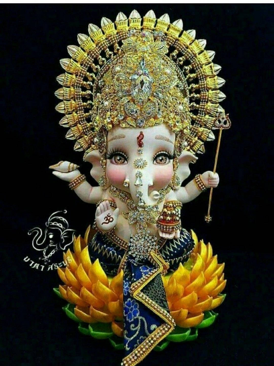 laxmi ganesh saraswati 桌布 壁紙 — 一尊裝飾華麗的象神雕像，頭戴金色皇冠珠寶，身穿藍色花卉服飾，坐在黑色背景前的金色蓮花上。