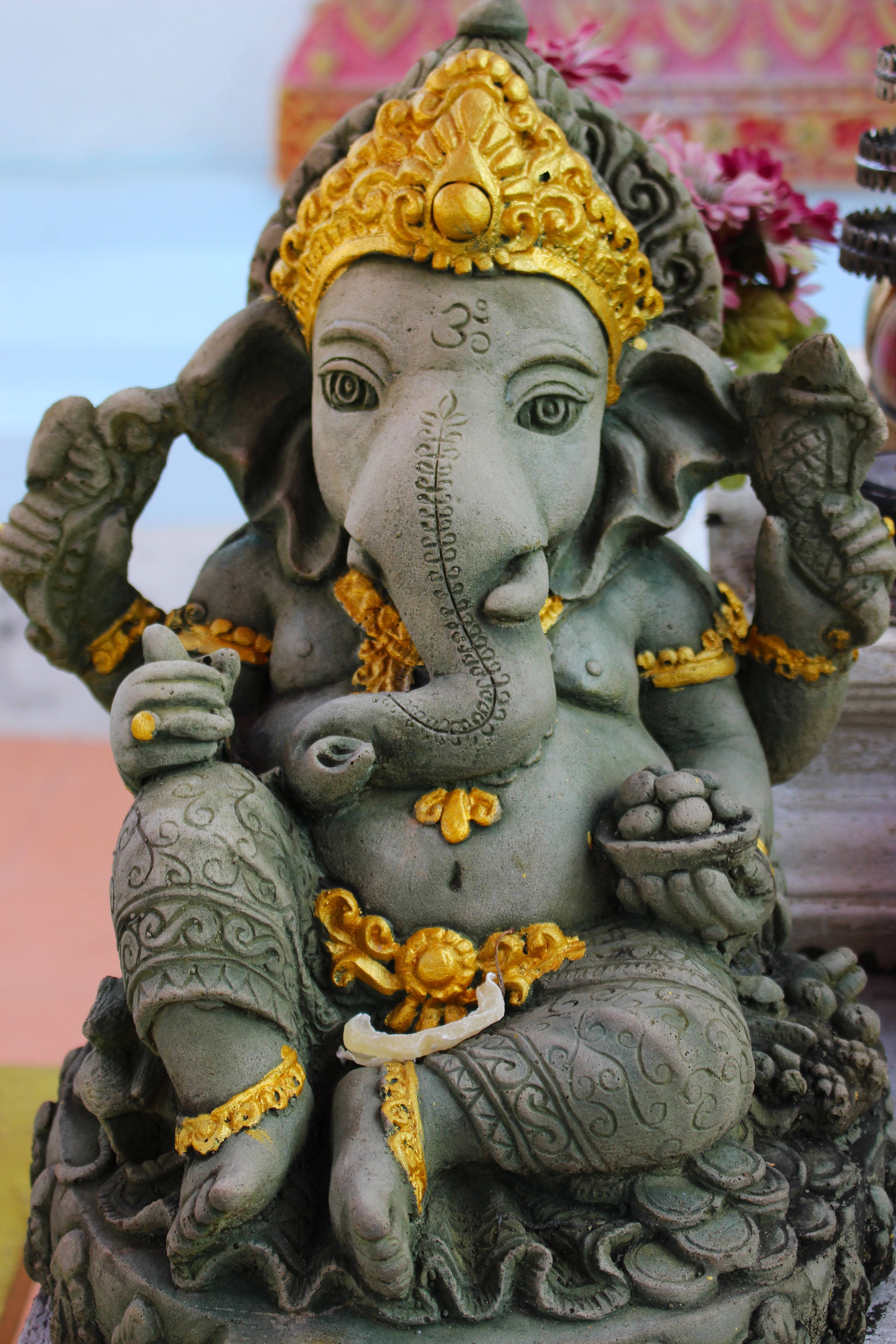 ganesh iPhone 桌布 壁紙 — 一尊詳細的石雕象頭神像，飾有金色裝飾，在寧靜的寺廟環境中手持象徵性物品。