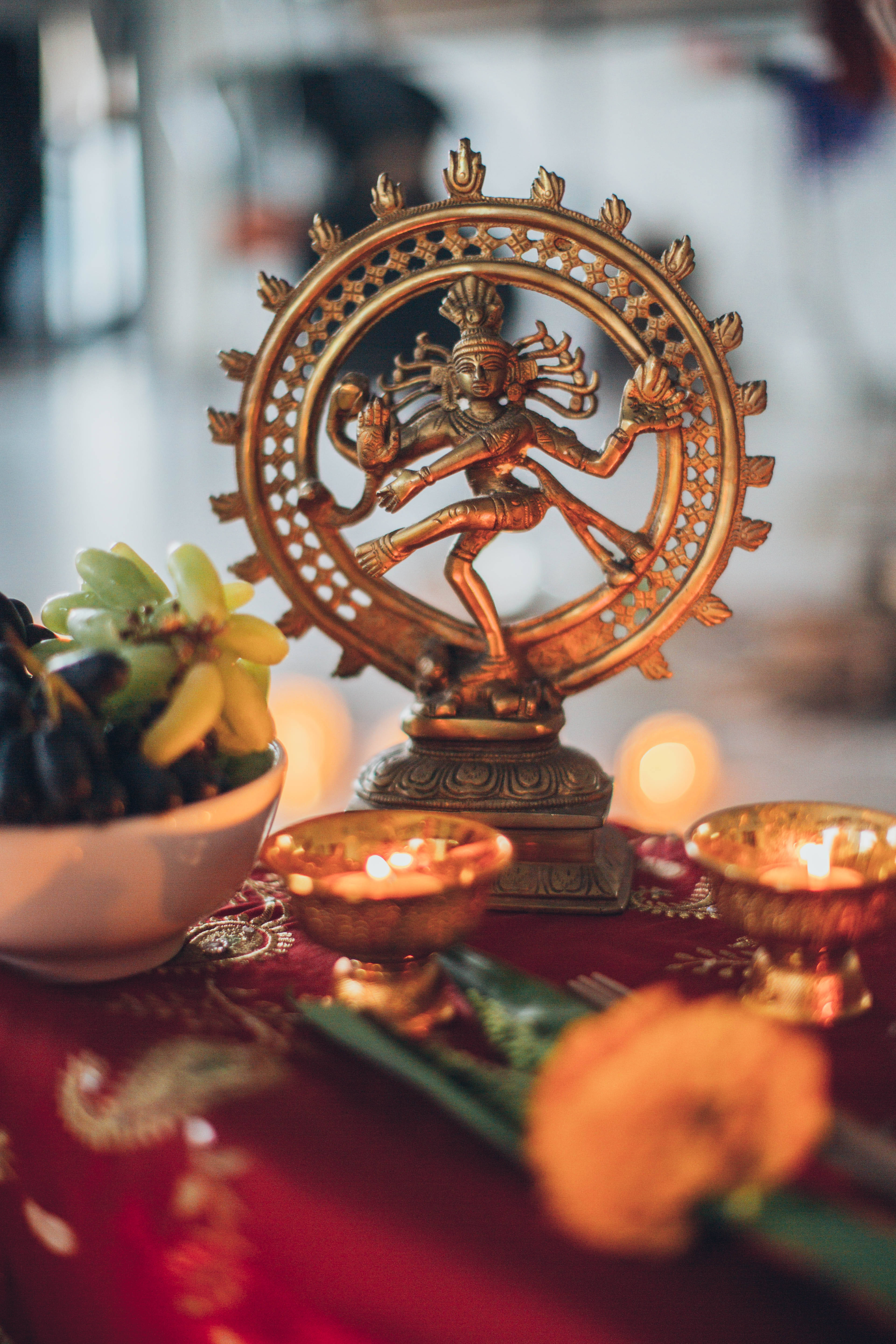 Lord Shiva 桌布 壁紙 — 一尊金色的濕婆納塔拉賈雕像在紅色布上的火環中跳舞，周圍環繞著點燃的油燈和新鮮花朵。