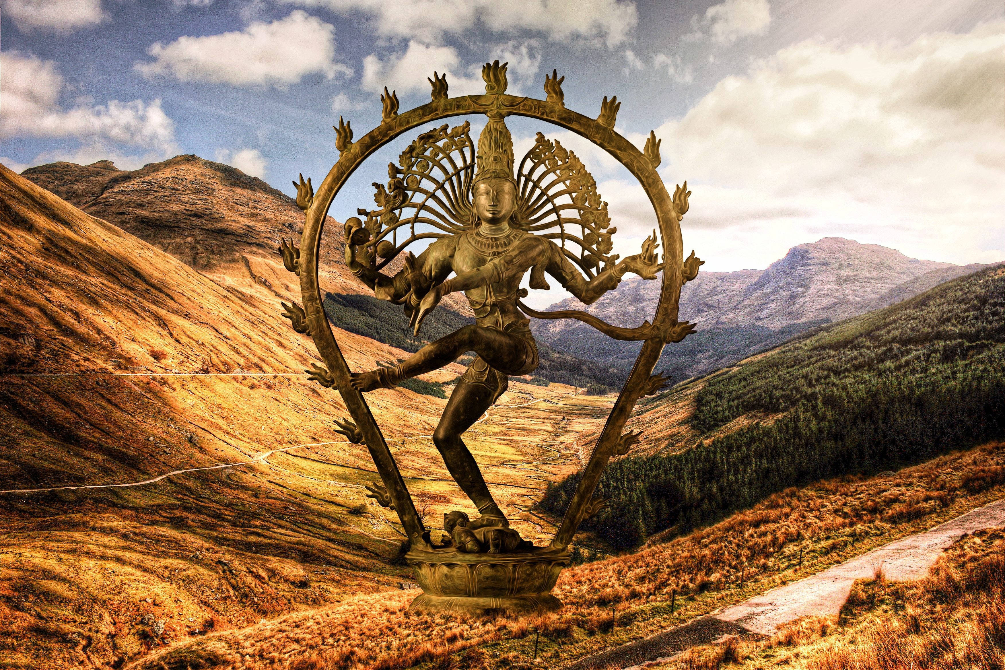 Lord Shiva 桌布 壁紙 — 一尊金色的濕婆納塔拉賈雕像在部分多雲的天空下，以崎嶇的山丘為背景，在山脊上跳舞。