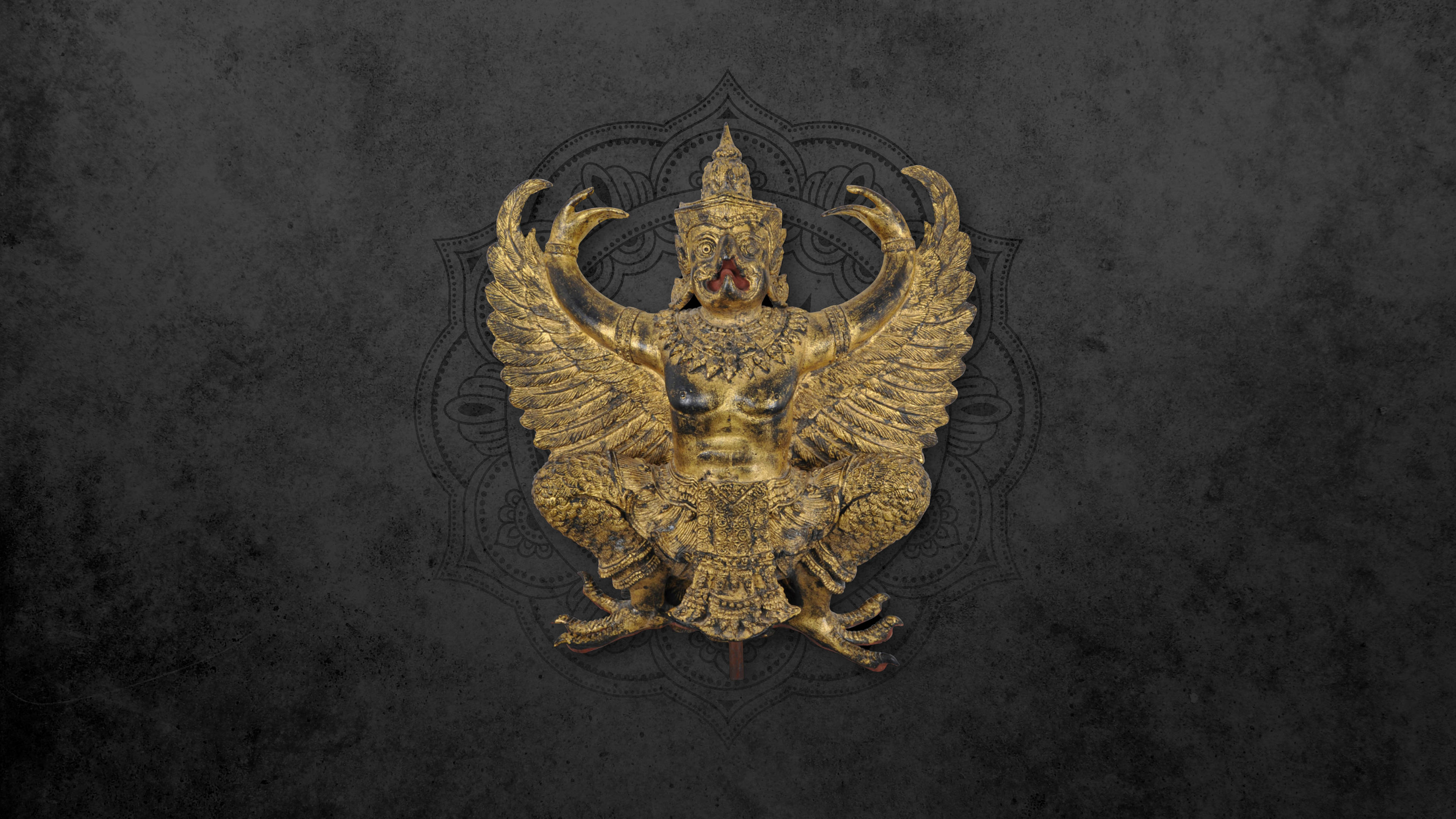 Garuda 桌布 壁紙 — 一尊金色華麗的迦樓羅雕像，翅膀展開，細節精緻，矗立在帶有微妙曼陀羅圖案的深色紋理背景前。