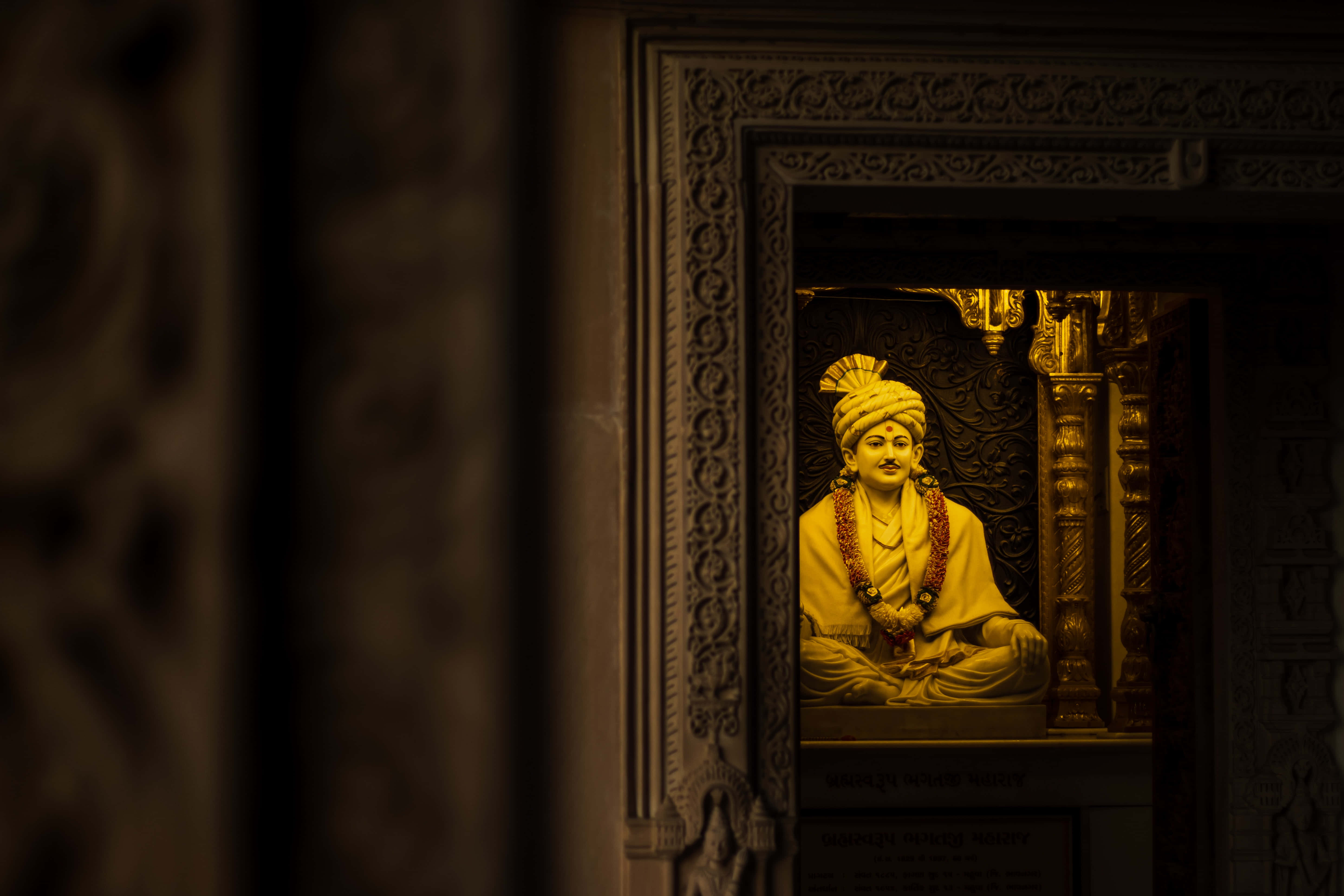 Shivaji Maharaj 桌布 壁紙 — 一尊金色雕像，描繪一位身穿華麗長袍的寧靜坐像，在雕刻精美的神龕壁龕中溫暖地發光。