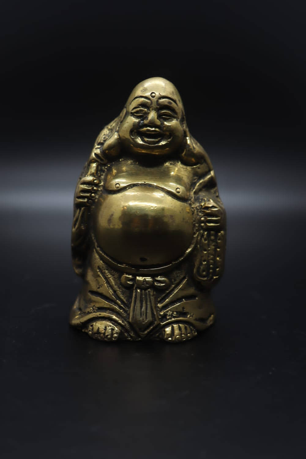 Statue Aesthetic 桌布 壁紙 — 一尊閃亮的黃銅佛像，帶著喜悅的表情，居中站立在深黑色背景前。