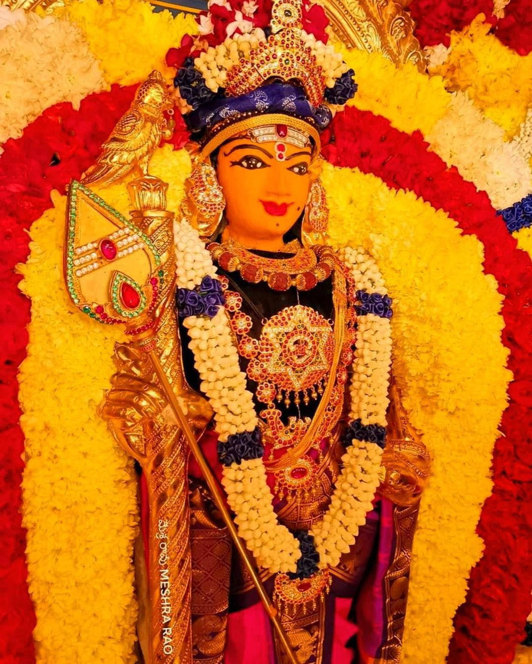 India 桌布 壁紙 — 一尊閃耀的印度教女神雕像，飾有黃金首飾和鮮豔的紅黃色花環。