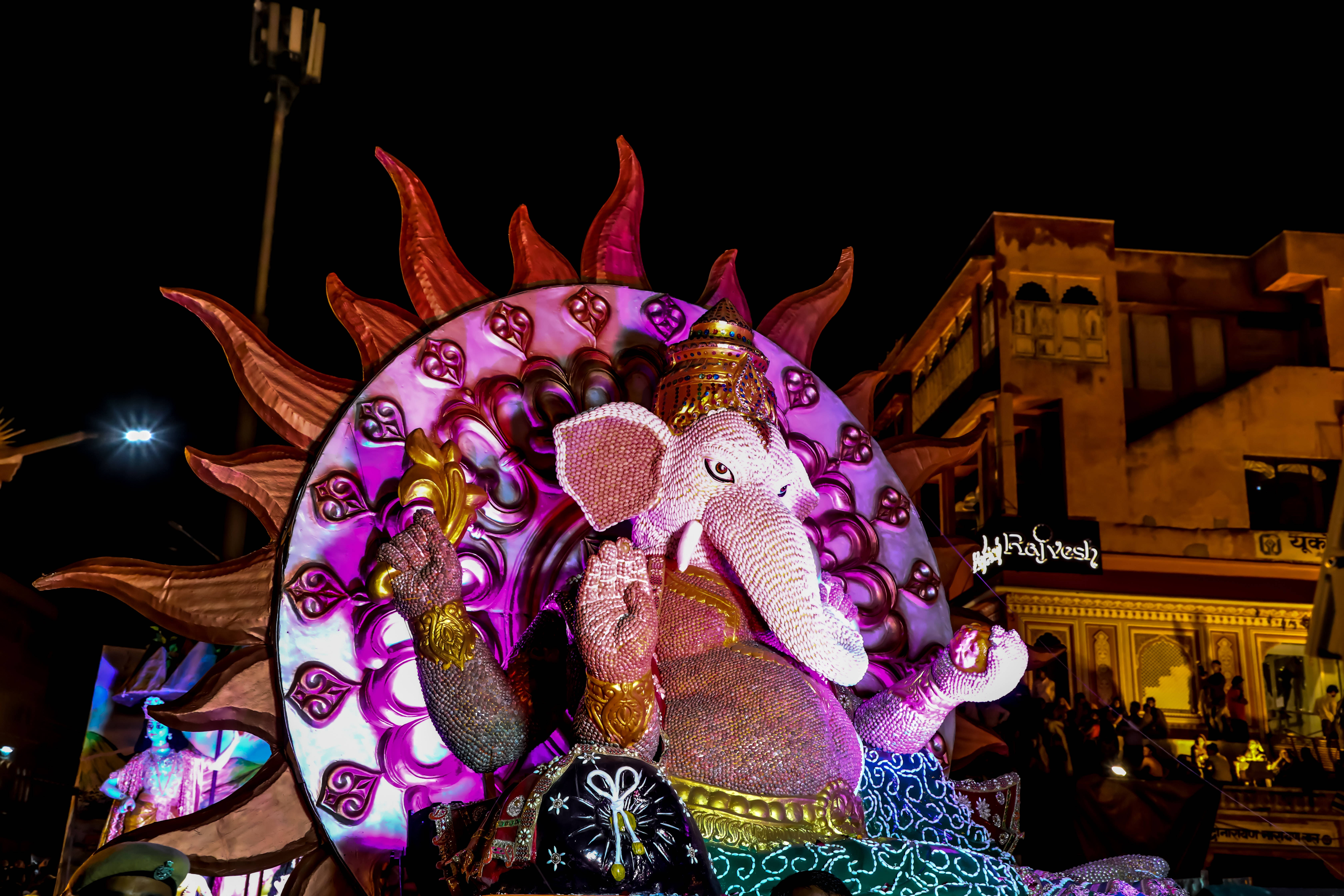 Ganesh 桌布 壁紙 — 一尊閃耀的象神雕像，配以粉紅和紫色燈光，在夜間街頭節日中散發光芒。