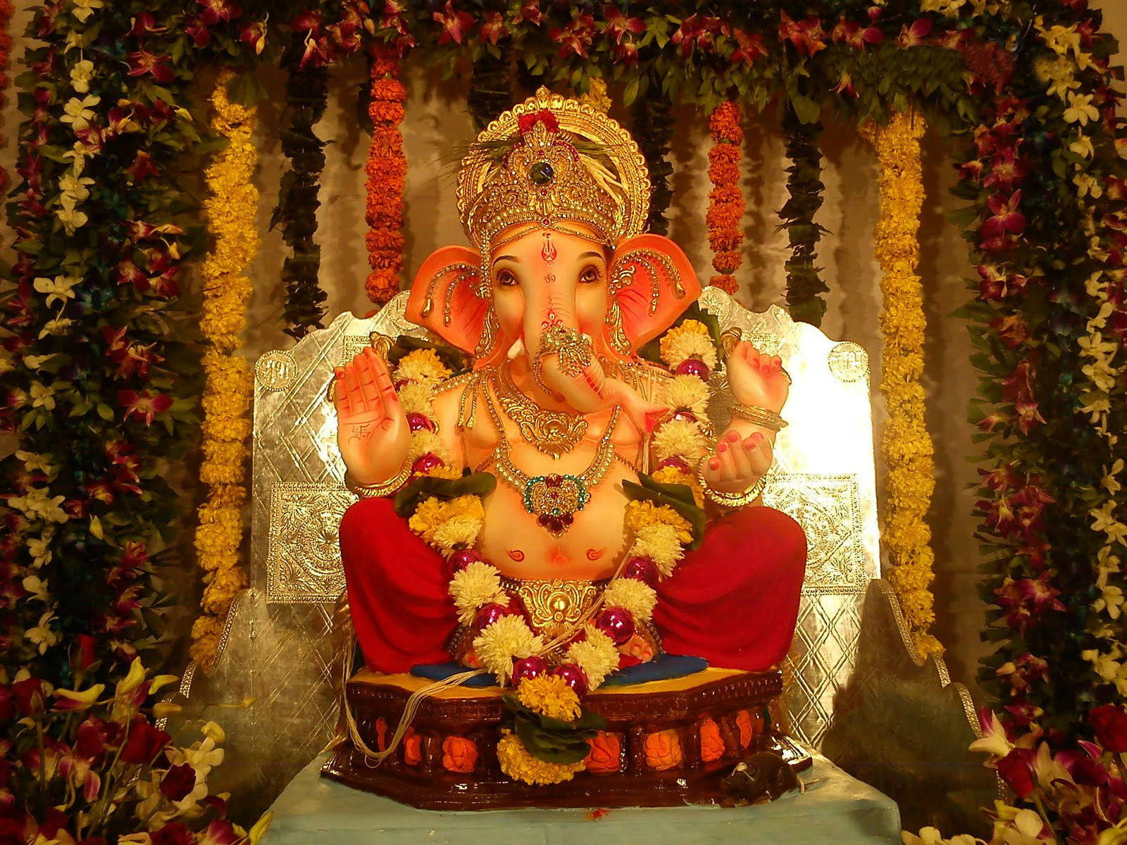 Ganesh 桌布 壁紙 — 一尊閃耀的金色象神像，飾以紅黃花朵，安坐於裝飾華麗的基座上。