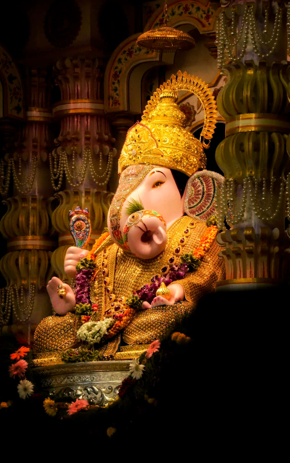 Ganesh Chaturthi 桌布 壁紙 — 一尊閃耀的金色象神像，飾以色彩繽紛的花朵和精緻珠寶，在寺廟環境中莊嚴地坐著。