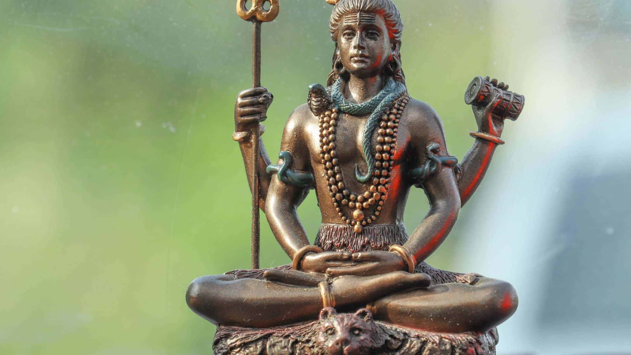Shiva 桌布 壁紙 — 一尊青銅濕婆神像，呈冥想姿態，手持三叉戟和鼓，背景為柔和綠色。