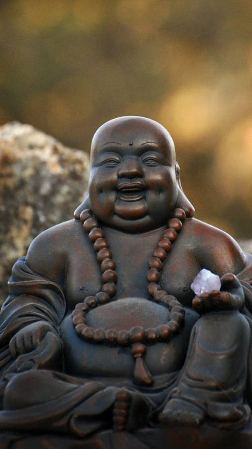 Statue Aesthetic 桌布 壁紙 — 一尊青銅笑佛雕像安詳地坐著，手持水晶，背景是模糊的岩石。