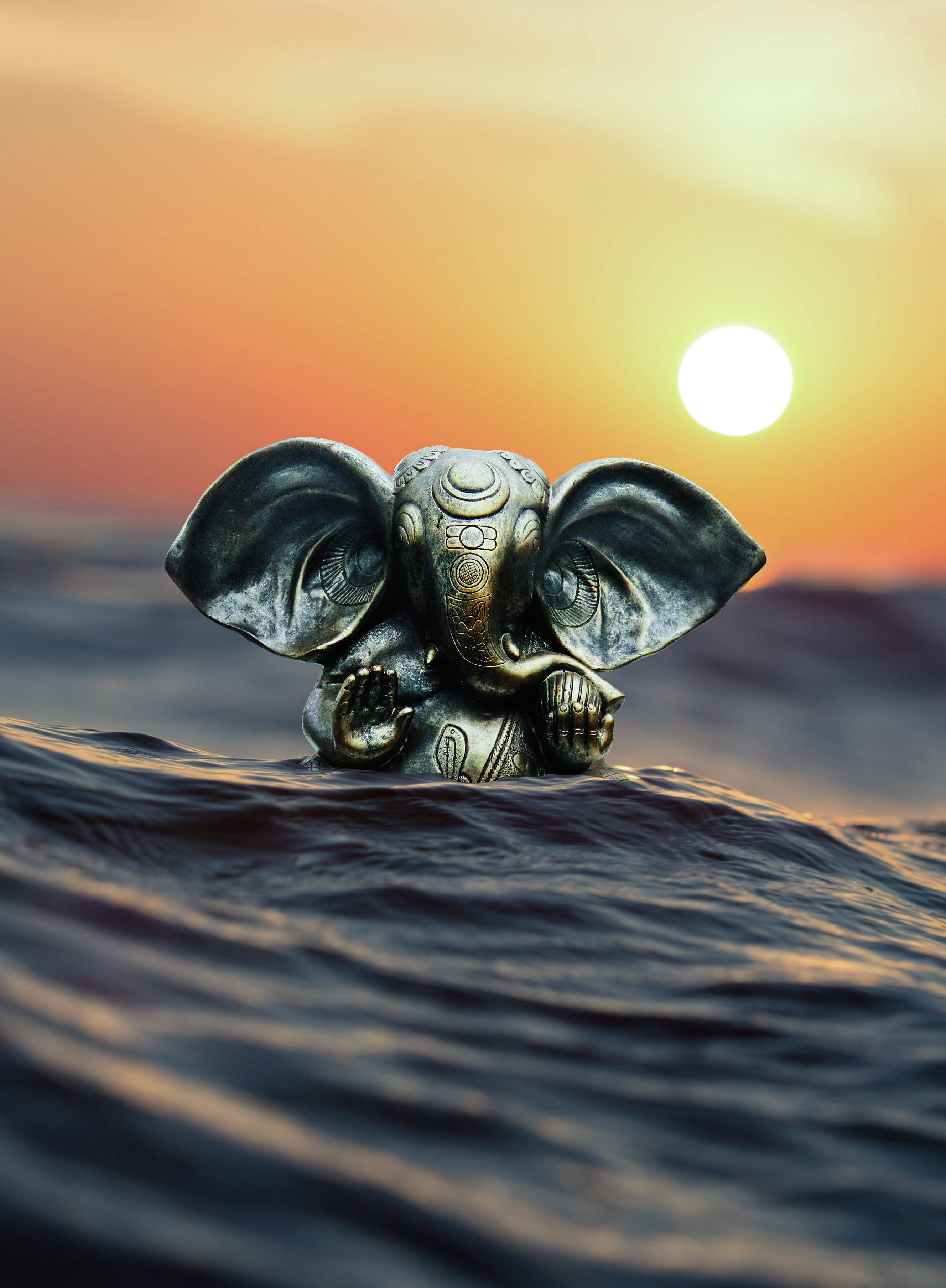 Ganesh 桌布 壁紙 — 一尊青銅象神雕像在日落時從海浪中浮現，背後有發光的太陽。