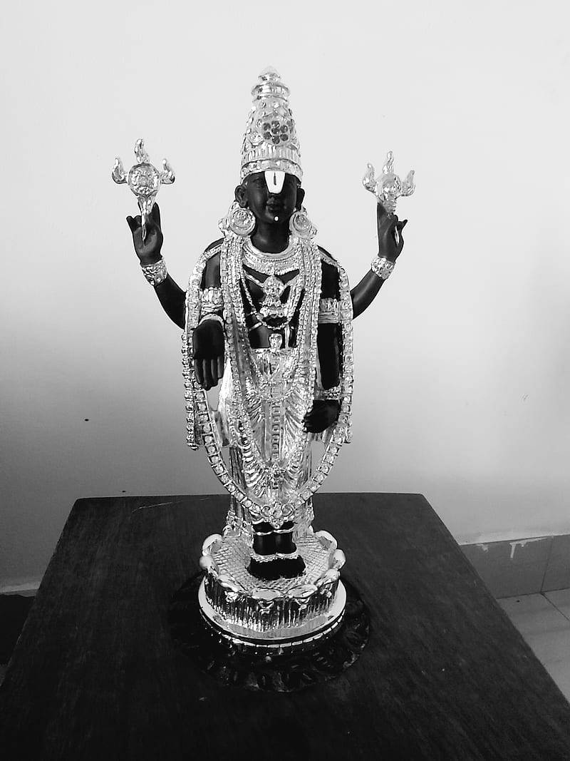 Vishnu 桌布 壁紙 — 一尊黑銀色的神像，飾有精緻珠寶，威嚴地立於深色木桌上，背景為素牆。