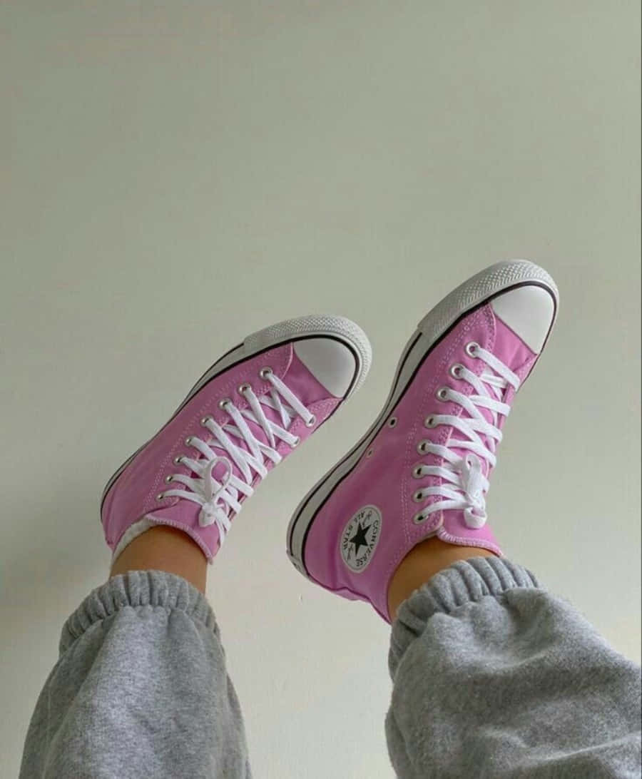 Pink Shoes 桌布 壁紙 — 一對亮粉紅色Converse運動鞋，配有白色鞋帶和橡膠鞋頭，搭配灰色運動褲，背景是素色牆壁。