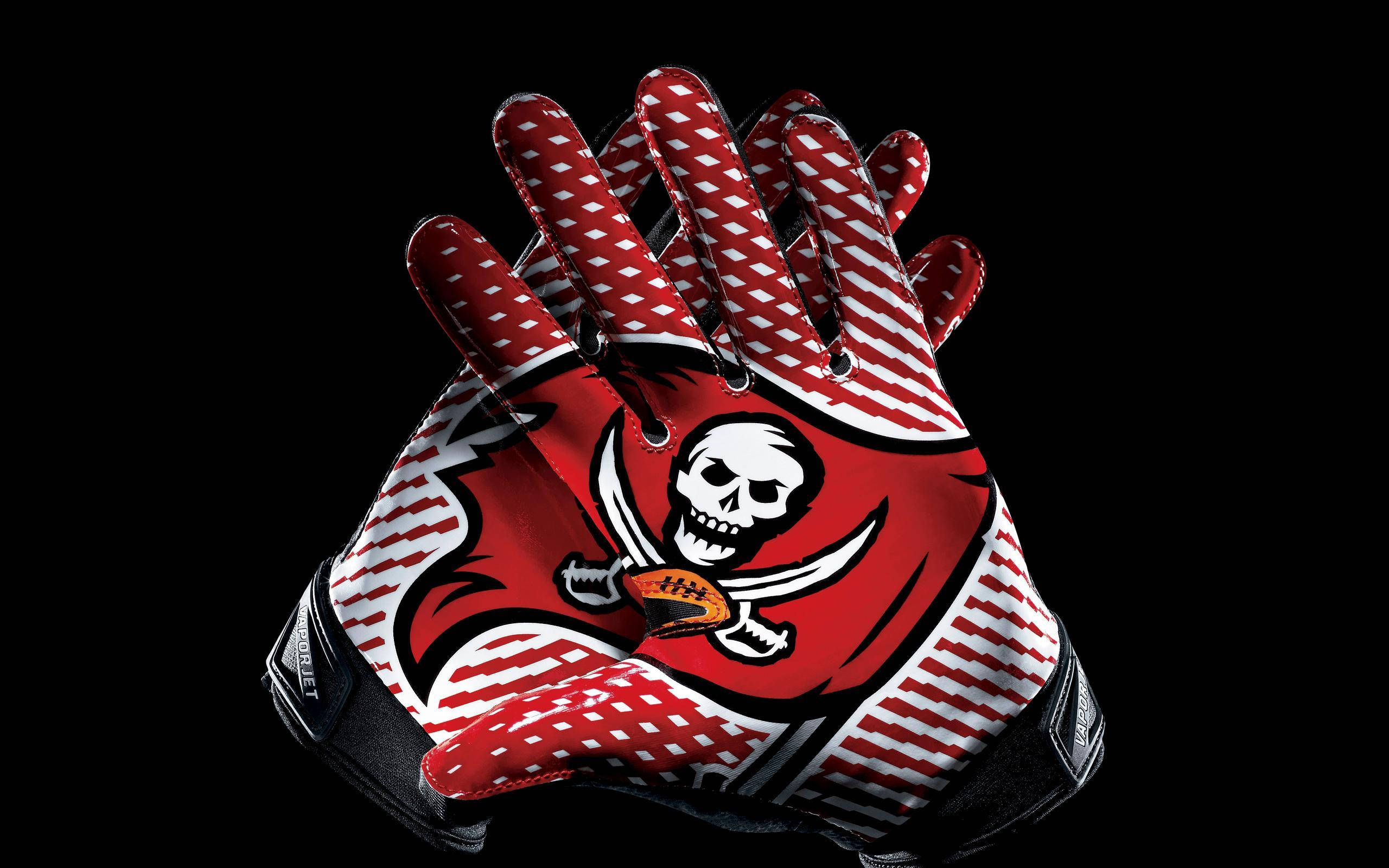 Buccaneers 桌布 壁紙 — 一對坦帕灣海盜隊美式足球手套，帶有骷髏頭和交叉劍標誌，背景為黑色。