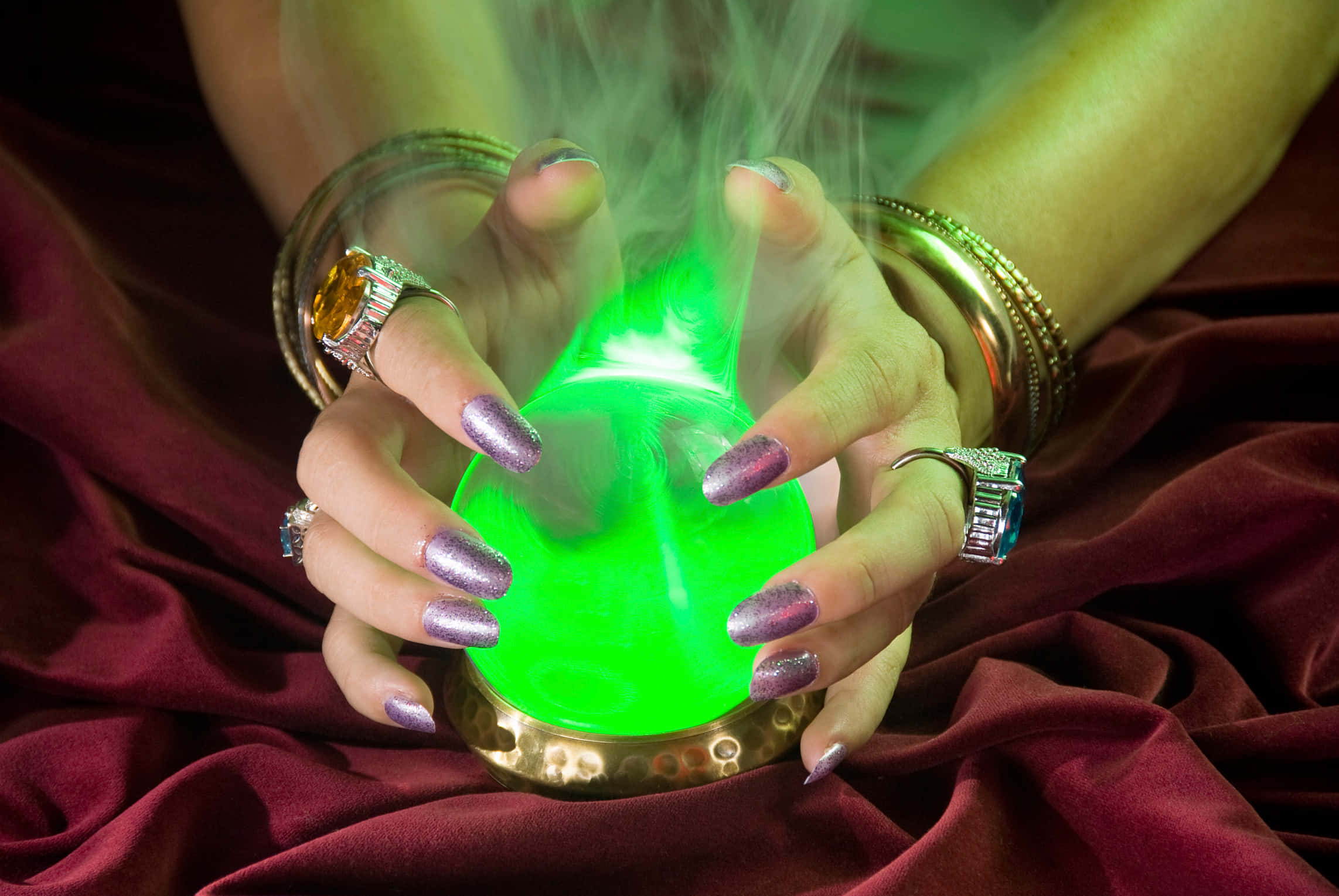Fortune Teller 桌布 壁紙 — 一對帶有閃亮指甲的手捧著一個發出神秘煙霧的發光綠色球體，背景是深紅色天鵝絨。