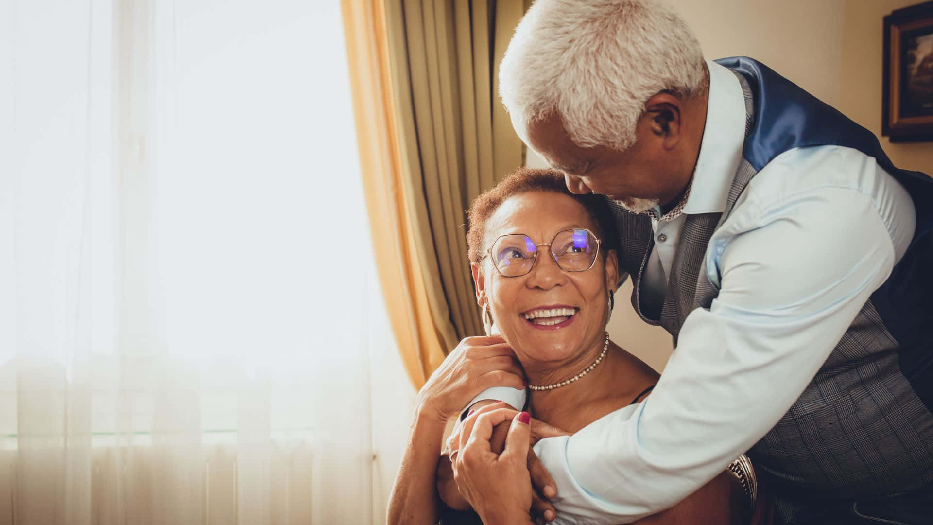 Beautiful Love 桌布 壁紙 — 一對年長夫婦在一個光線溫暖、帶有柔軟窗簾和金色色調的房間裡溫柔擁抱。