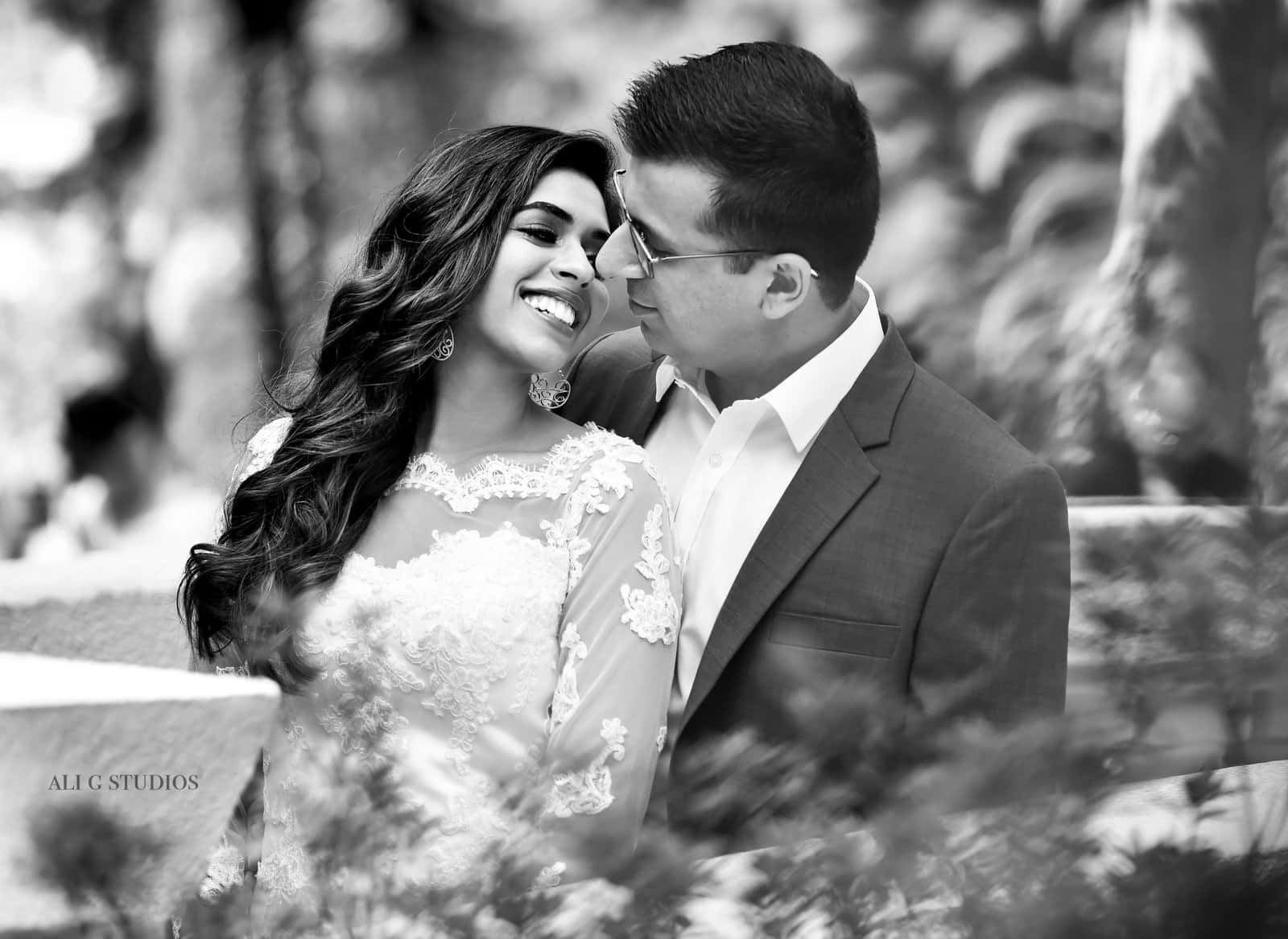 Black And White Wedding 桌布 壁紙 — 一對微笑的情侶在戶外分享親密時刻的黑白肖像，背景是模糊的樹葉。