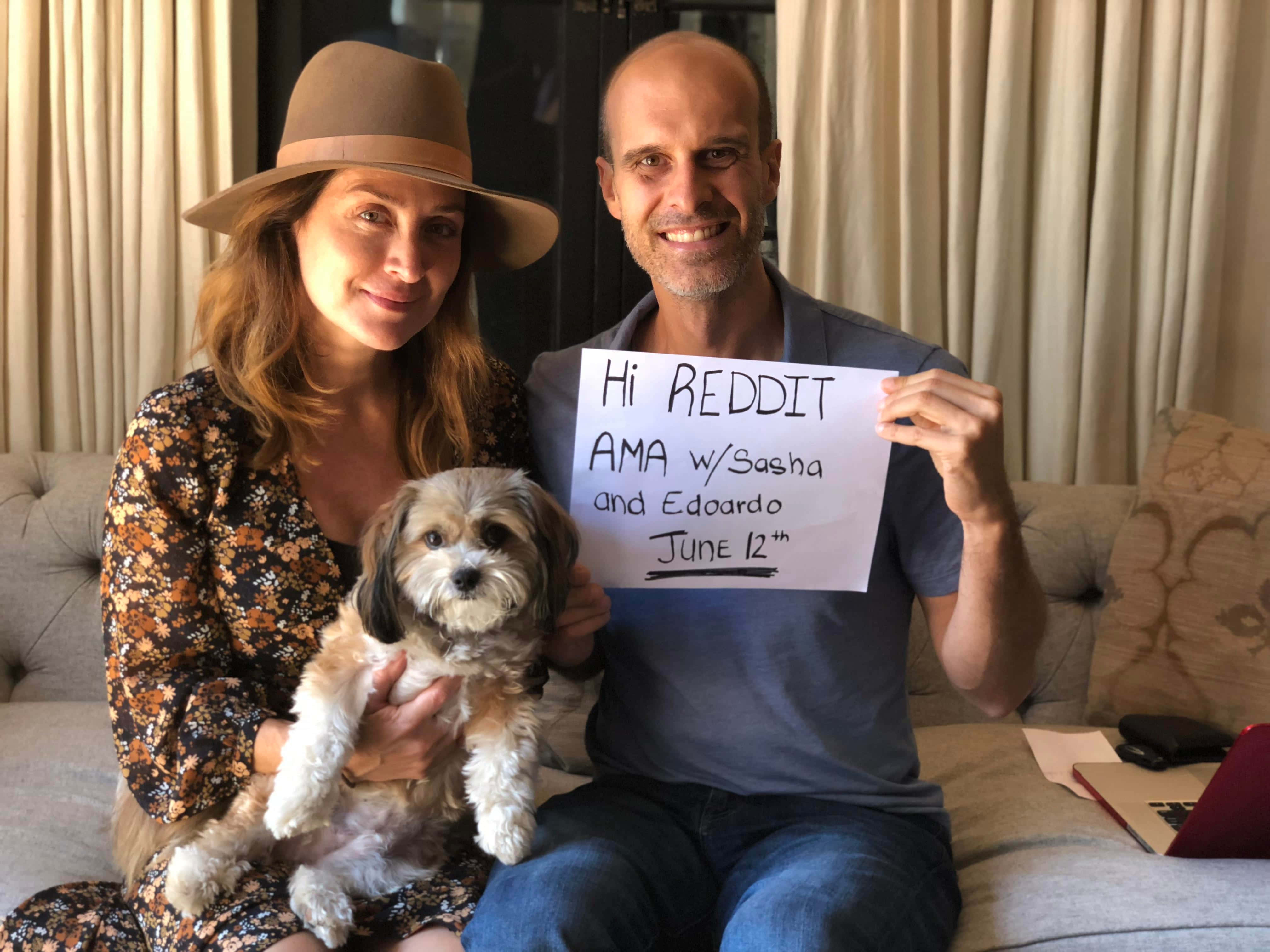 Sasha Alexander 桌布 壁紙 — 一對微笑的情侶坐在沙發上，帶著一隻毛茸茸的小狗，男子手持手寫標語宣布在Reddit上進行AMA。
