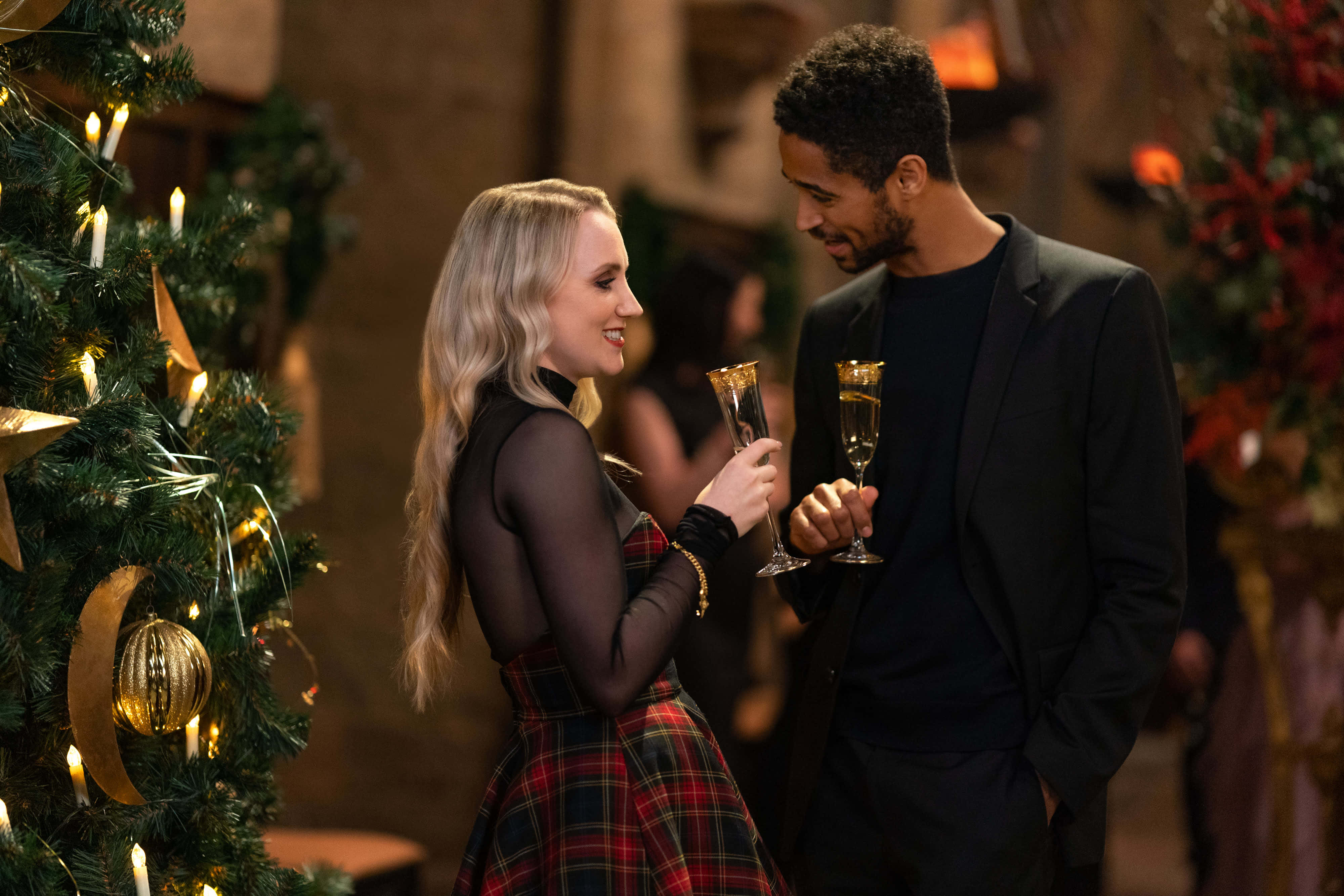 Harry Potter Christmas 桌布 壁紙 — 一對微笑的情侶穿著節日服裝，在溫暖燈光的室內環境中，在裝飾好的聖誕樹旁碰杯香檳。