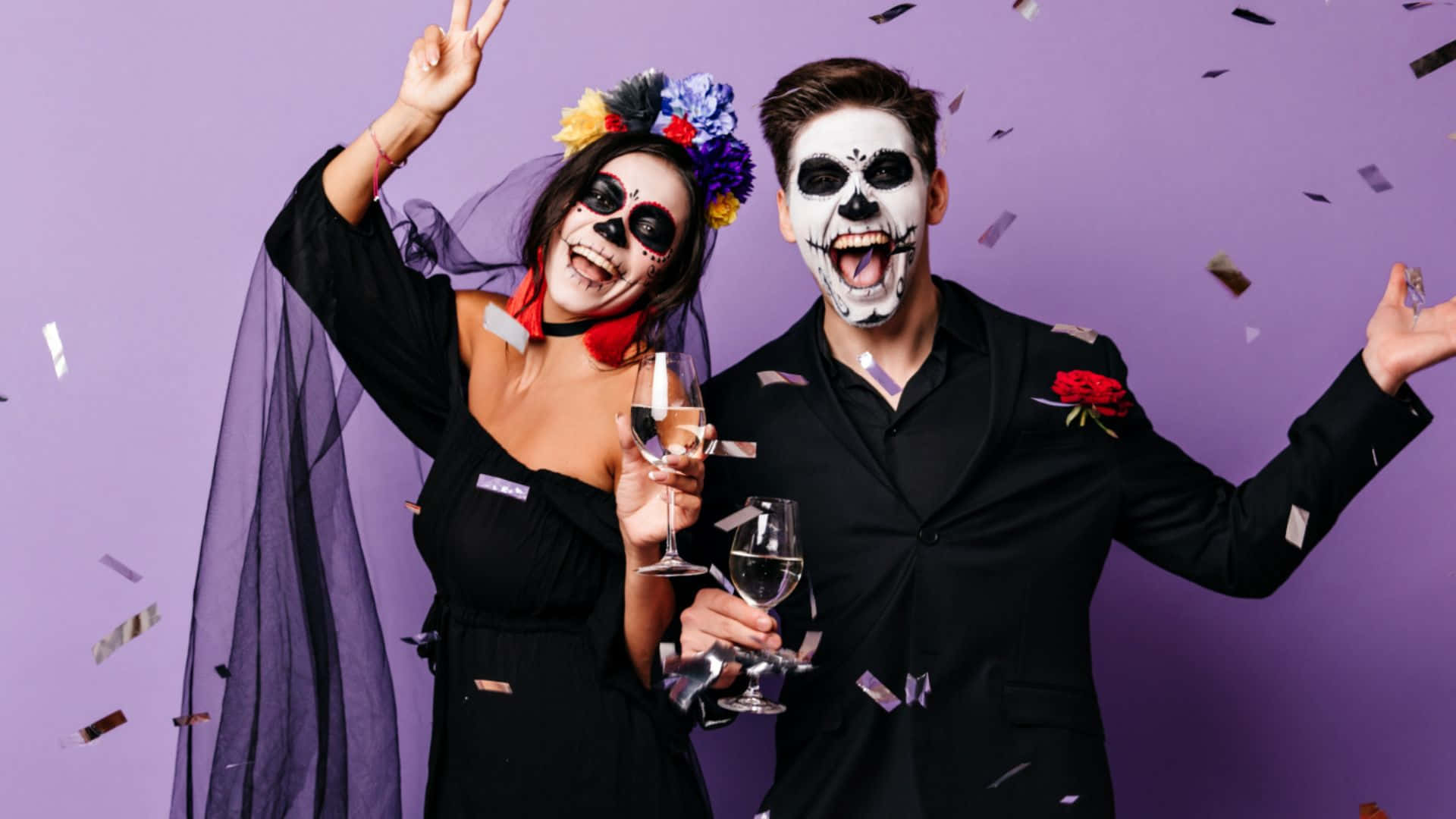 Halloween Costumes 桌布 壁紙 — 一對快樂的情侶以糖骷髏化妝，在紫色背景上灑滿五彩紙屑，用香檳慶祝。