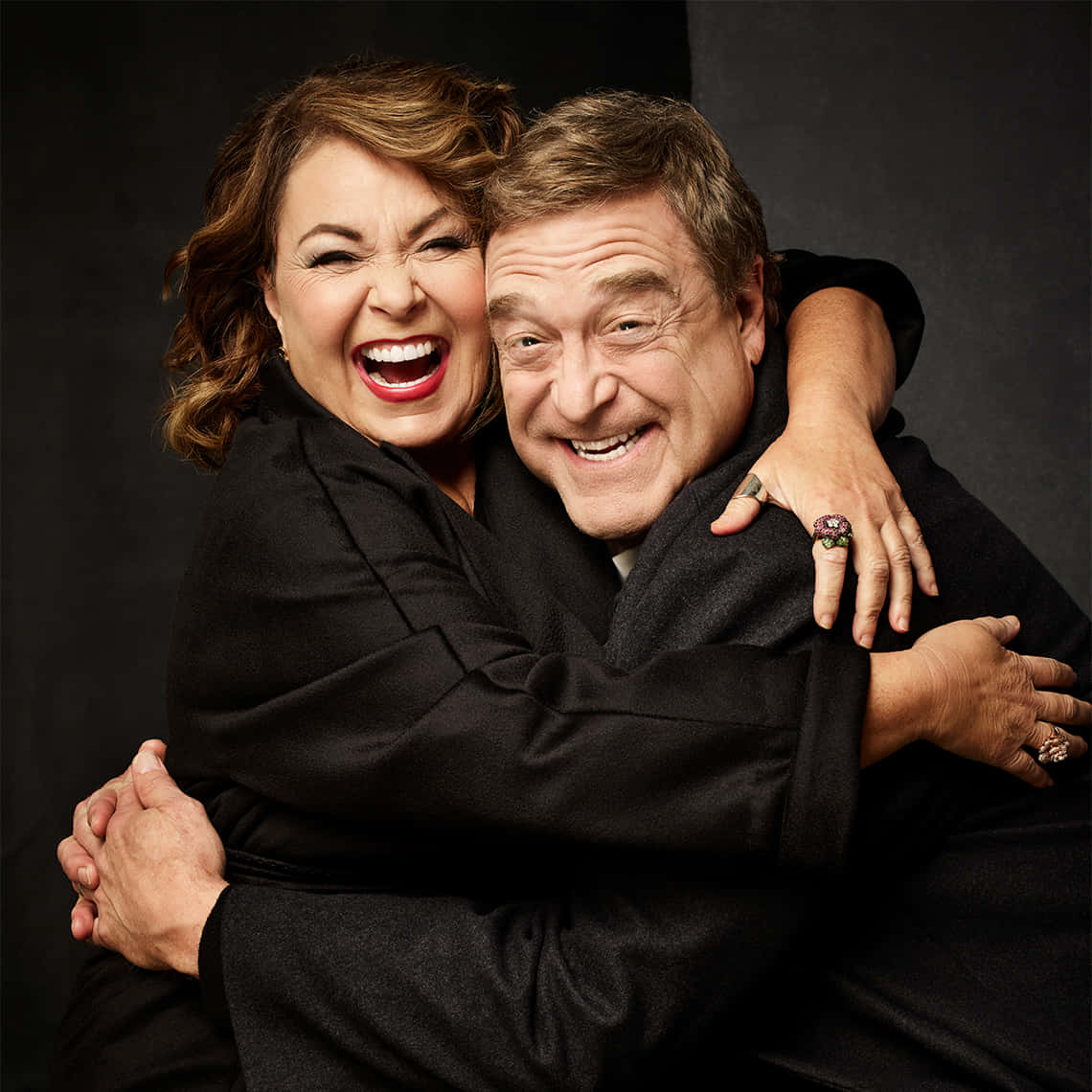John Goodman 桌布 壁紙 — 一對快樂的情侶在黑暗背景下緊緊擁抱，兩人都張大嘴巴笑著，眼睛閃閃發光。