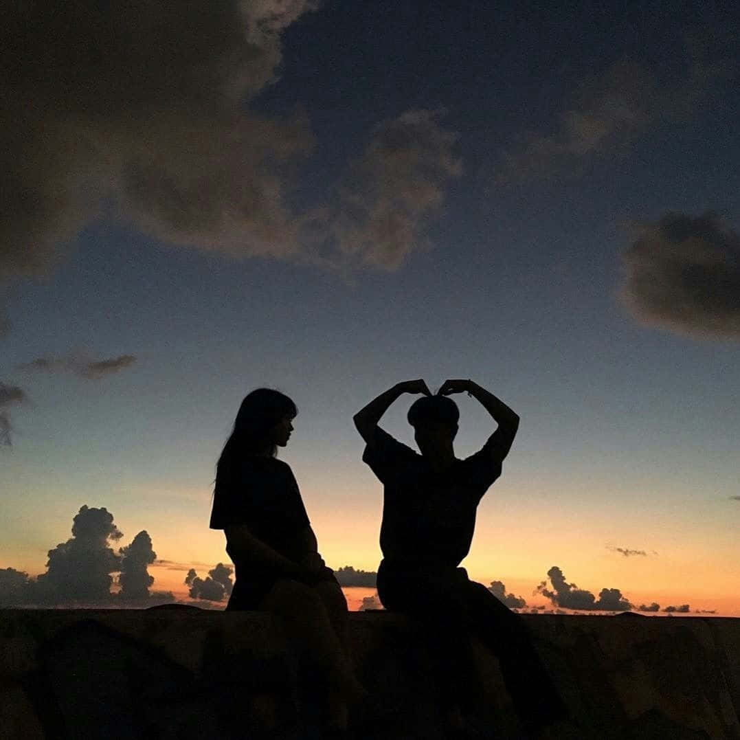 兩個人以日落天空為背景的剪影，其中一人用手比出心形。