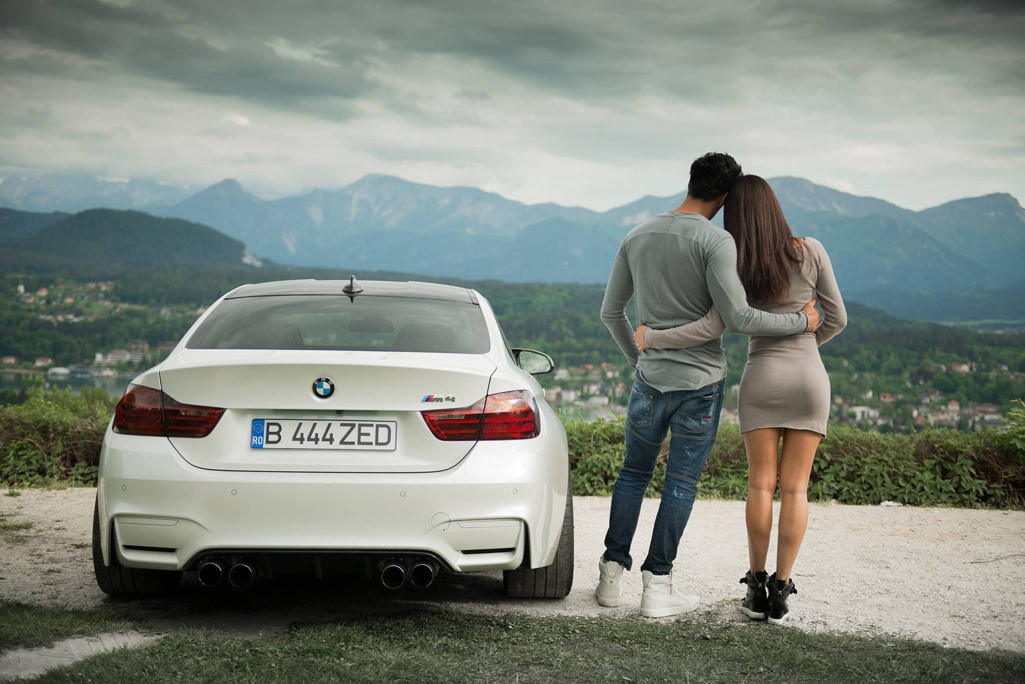 Sports Car 桌布 壁紙 — 一對情侶喺白色BMW M4旁邊擁抱，凝視住多雲天空下嘅遠山。