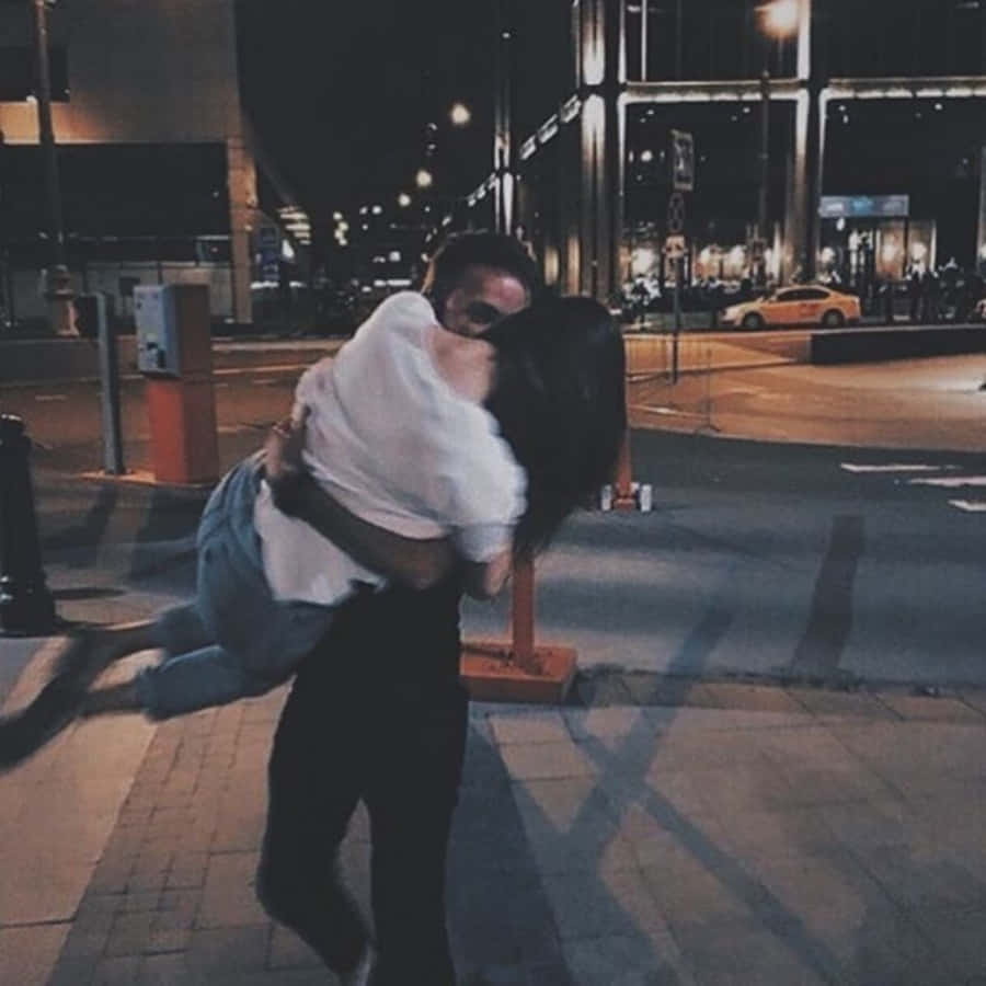 Cute Boyfriend 桌布 壁紙 — 一對情侶在夜間溫暖街燈下的城市行人道上熱情擁抱，背景是模糊的城市景觀。