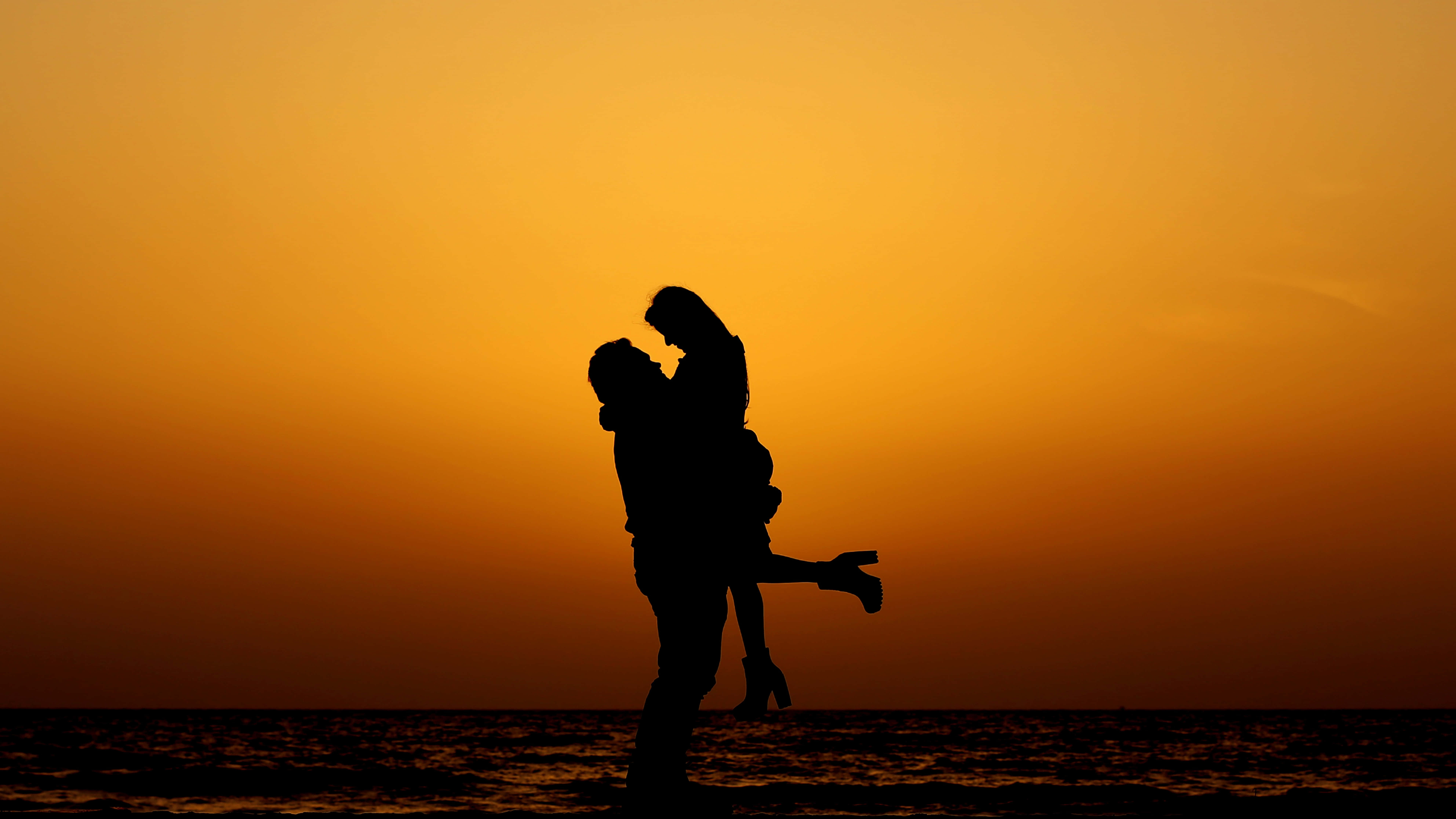 Beach Love 桌布 壁紙 — 一對情侶在海洋上溫暖的橙色日落中擁抱親吻的浪漫剪影。