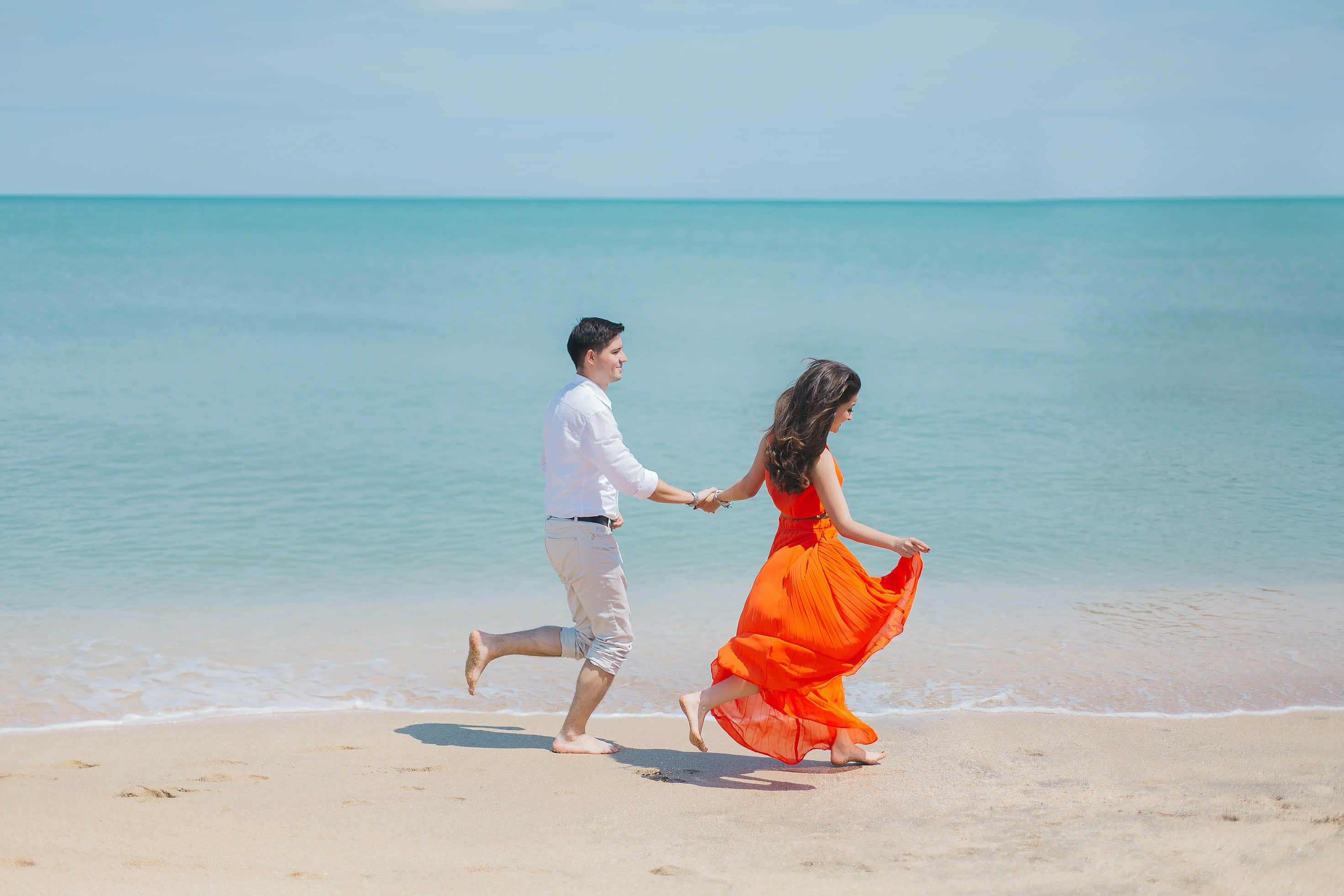 Beach Love 桌布 壁紙 — 一對情侶手牽手沿著陽光明媚的海灘奔跑，碧綠的海浪輕輕拍打著金色的沙灘。