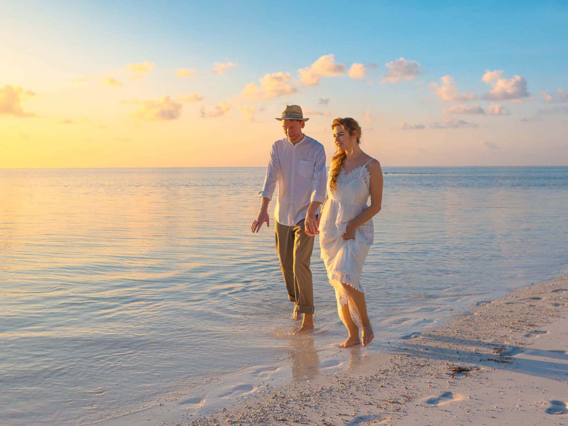 Beach Lovers 桌布 壁紙 — 一對情侶手牽手漫步在金色日落時分的寧靜海灘上，海水平靜，沙灘柔軟。