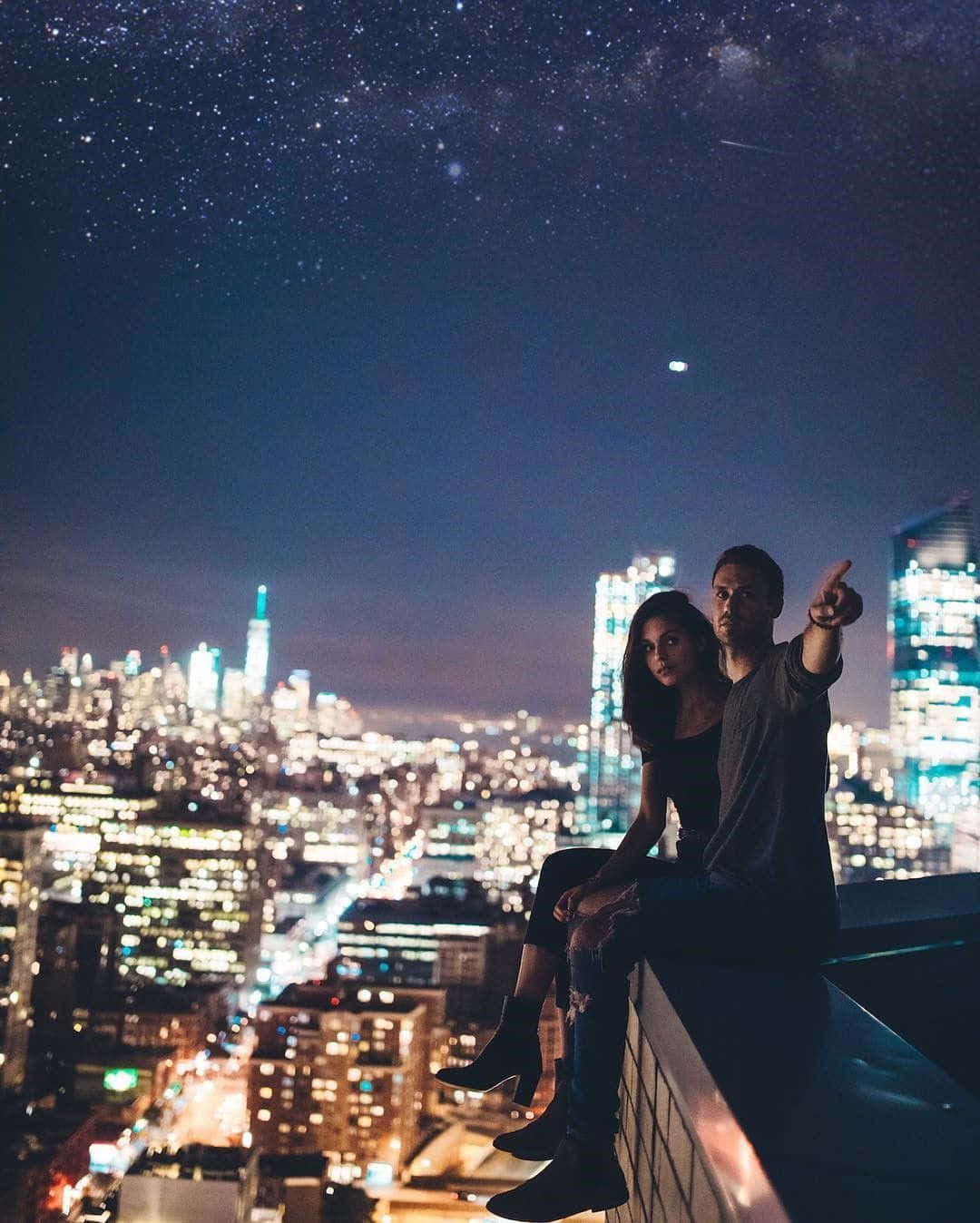 情侶在屋頂上指著城市燈光上方的星星