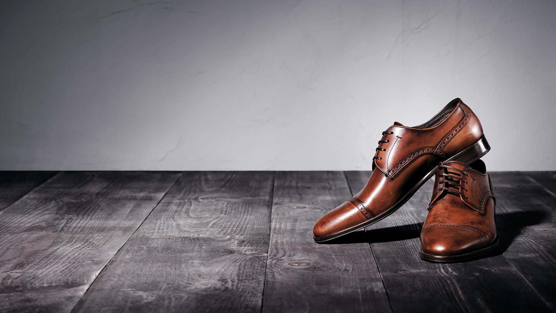Footwear Design 桌布 壁紙 — 一對拋光棕色皮革正裝鞋放在深色木板上，背景是帶紋理的灰色牆壁。