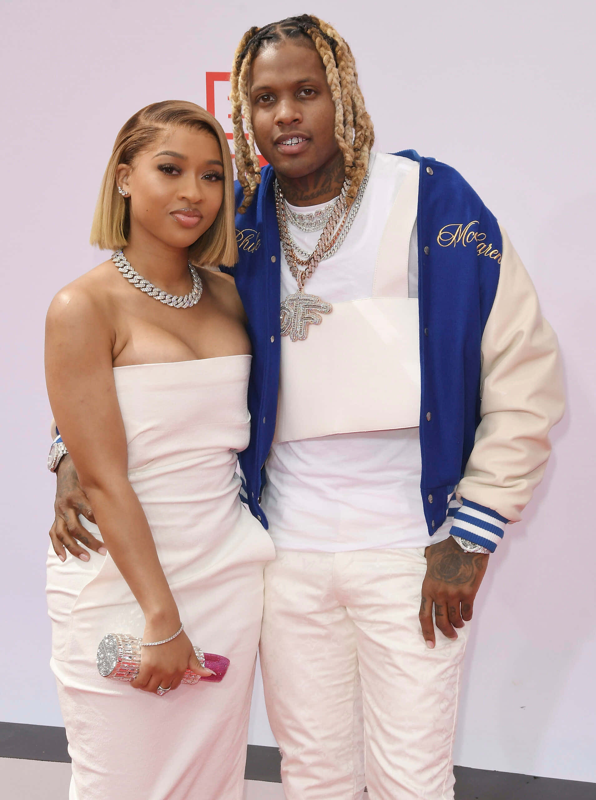 lil durk 桌布 壁紙 — 一對時尚情侶在紅地毯活動上自信地擺姿勢，穿著相配的白色服裝和閃亮的珠寶。