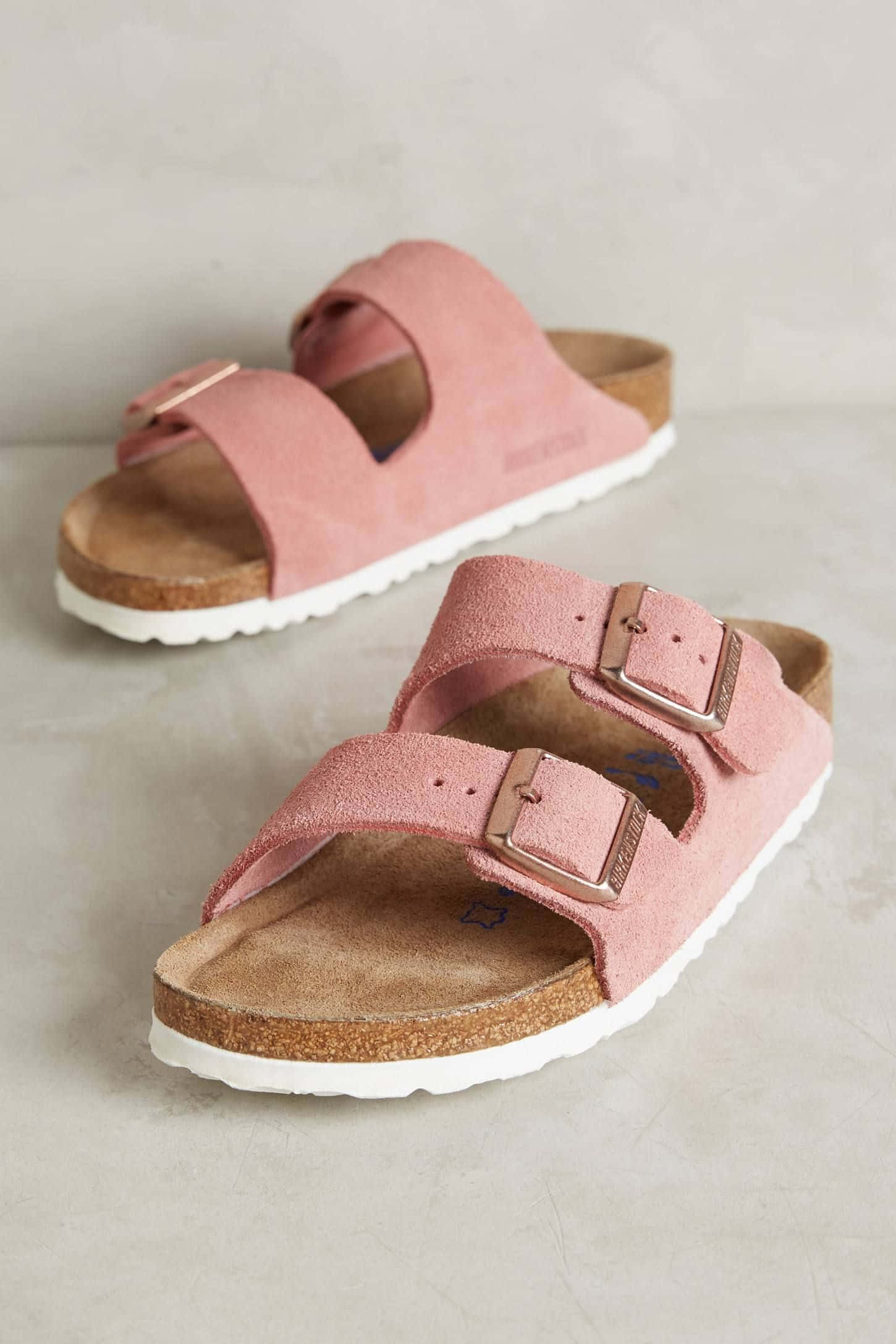 Sandals 桌布 壁紙 — 一對柔軟的粉紅色麂皮Birkenstock涼鞋，帶有金屬扣環，放在中性混凝土表面上。