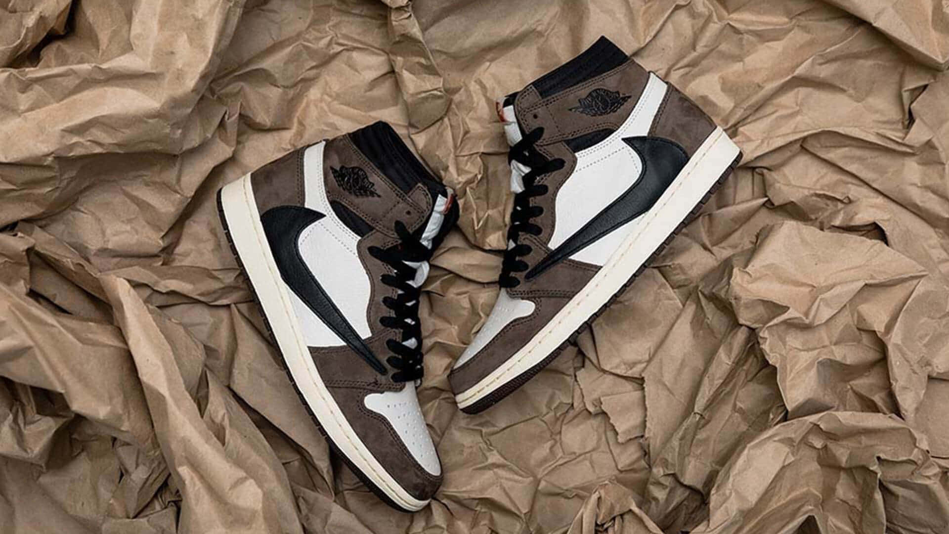 Travis Scott Jordan 1 桌布 壁紙 — 一對棕色、白色和黑色的高筒運動鞋放在帶有紋理細節的皺巴巴棕色紙上。