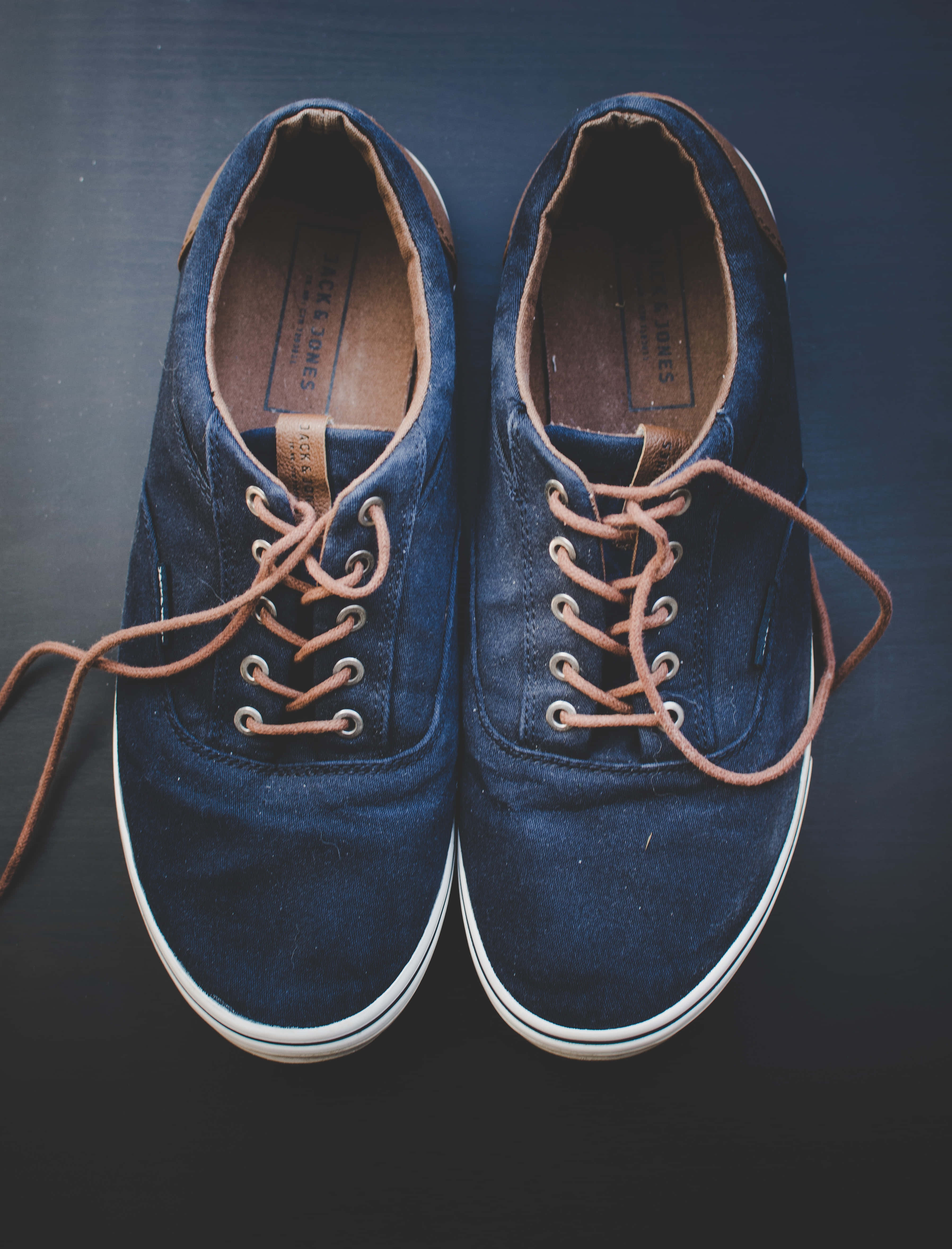 Navy Blue Shoes 桌布 壁紙 — 一對海軍藍絨面革運動鞋搭配棕褐色鞋帶，放置在深色表面上，展現經典休閒風格。