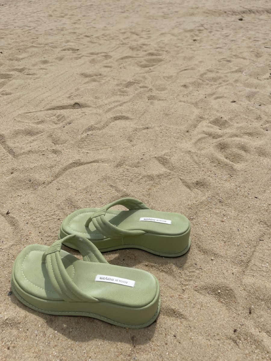 Beach Sandals 桌布 壁紙 — 一對淺綠色厚底涼鞋在明亮的日光下放置在質感沙地上。
