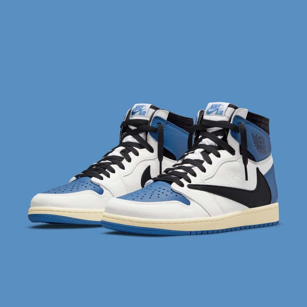 Travis Scott Jordan 1 桌布 壁紙 — 一對白色、藍色和黑色的高筒運動鞋，搭配奶油色鞋底，置於純藍色背景前。
