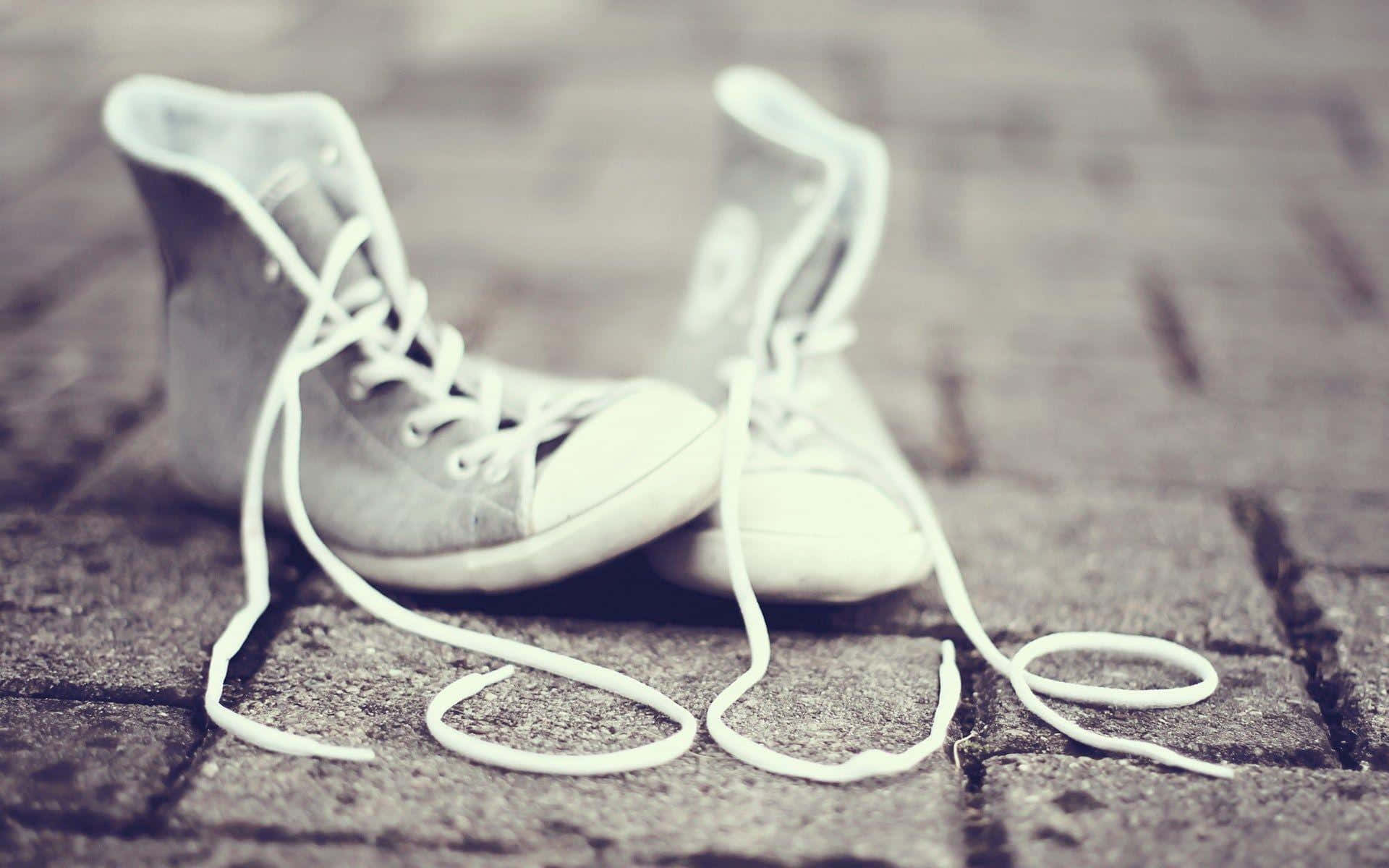 Cute Shoes 桌布 壁紙 — 一對白色高筒運動鞋，鞋帶鬆開，靜置在風化的鵝卵石街道上，色調柔和低沉。