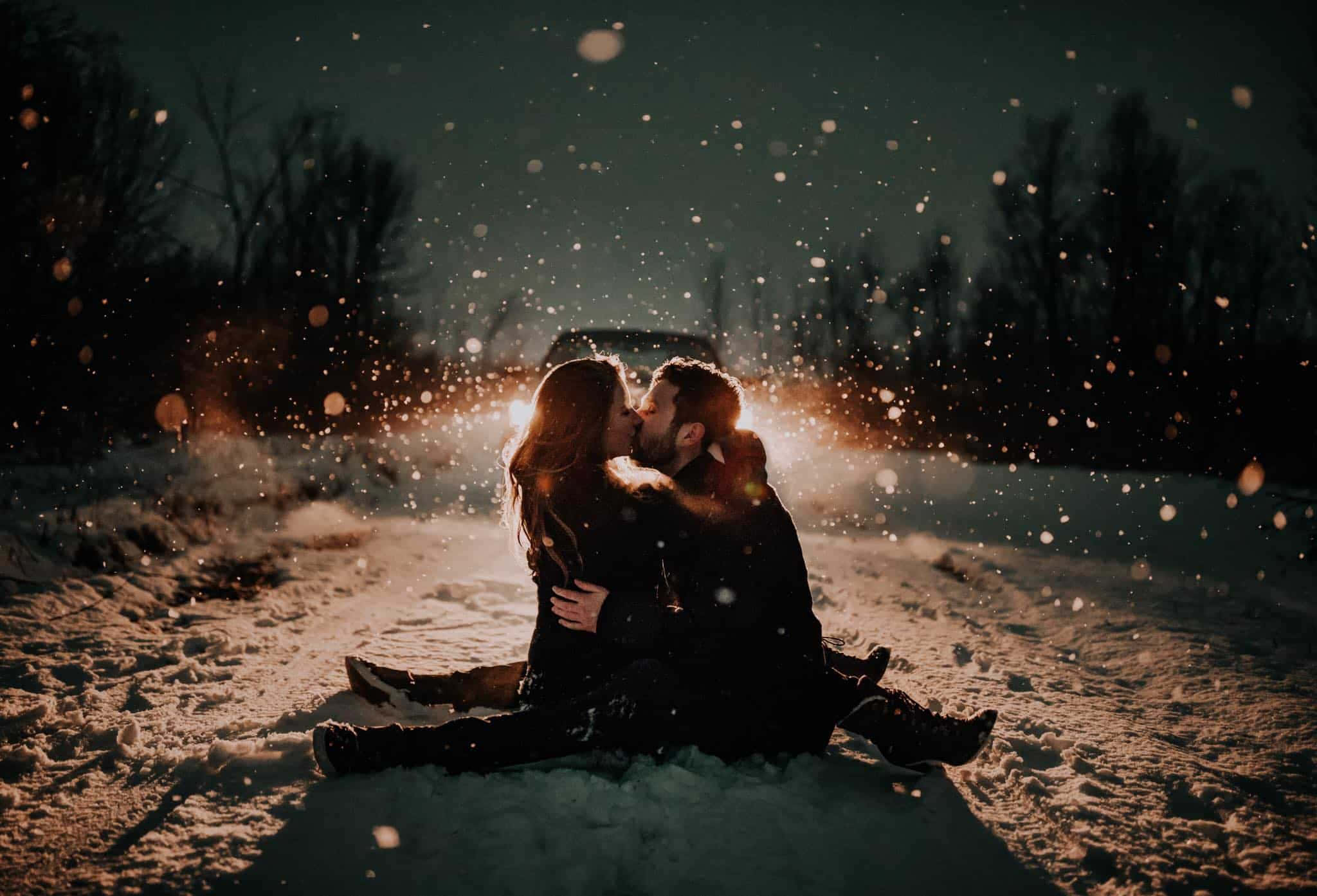 一對相愛的情侶 壁紙 — 一對情侶在飄雪中親吻，溫暖的背光映襯著黑暗的冬日景色。