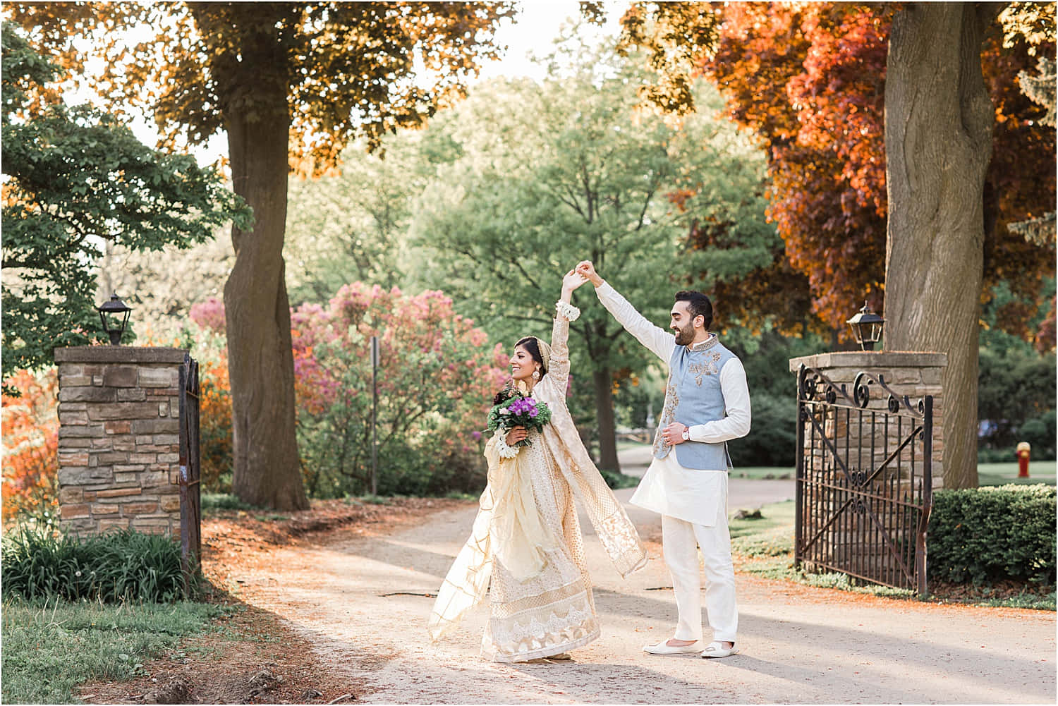 Garden Wedding 桌布 壁紙 — 一對穿著傳統服飾的情侶在陽光明媚的小徑上快樂地跳舞，小徑兩旁是色彩鮮豔的橙色和綠色秋葉樹木。