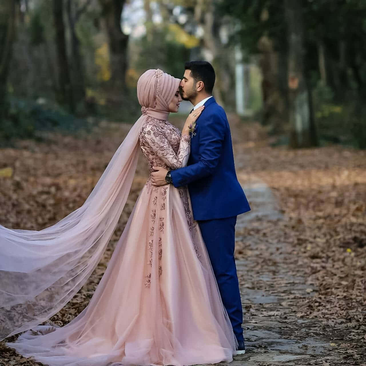 Wedding Couple 桌布 壁紙 — 一對穿著優雅婚紗的情侶在柔和秋光下，於落葉鋪滿的林間小徑上溫柔擁抱。