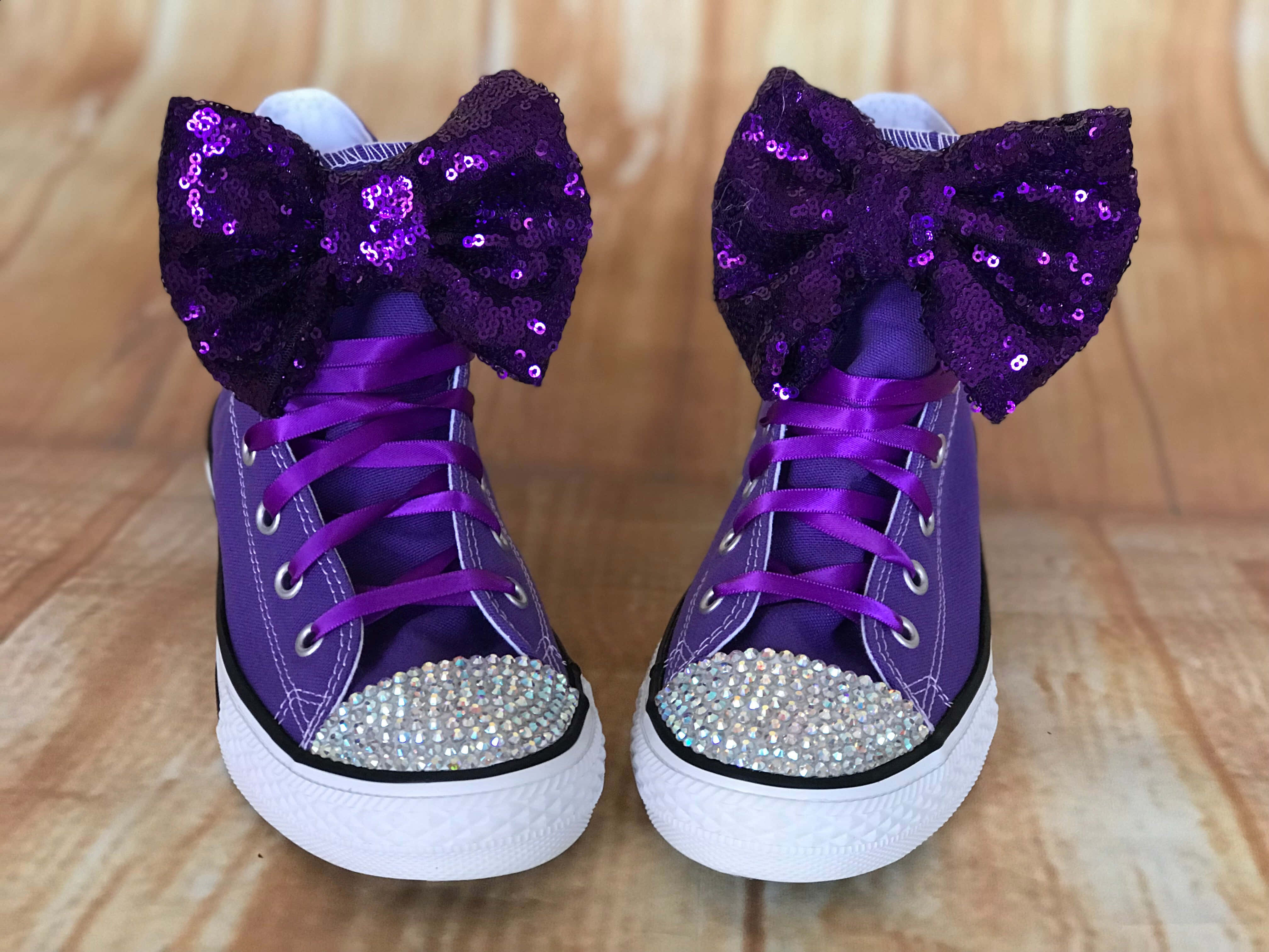 Purple Shoes 桌布 壁紙 — 一對紫色高筒運動鞋，帶有閃粉蝴蝶結和水鑽鞋頭，放在木地板上。
