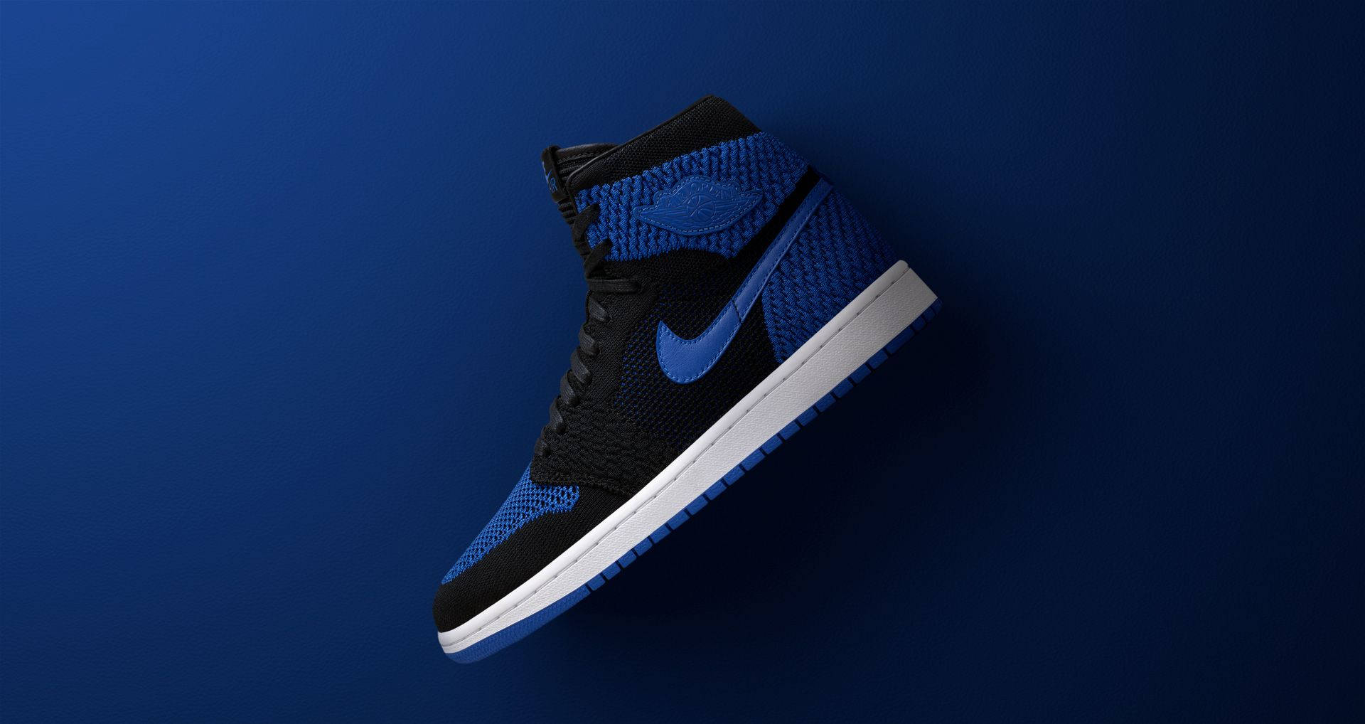 Nike Air Jordan 1 桌布 壁紙 — 一對高筒運動鞋，黑色和皇家藍色針織鞋面，白色鞋底，靠在純深藍色背景上。