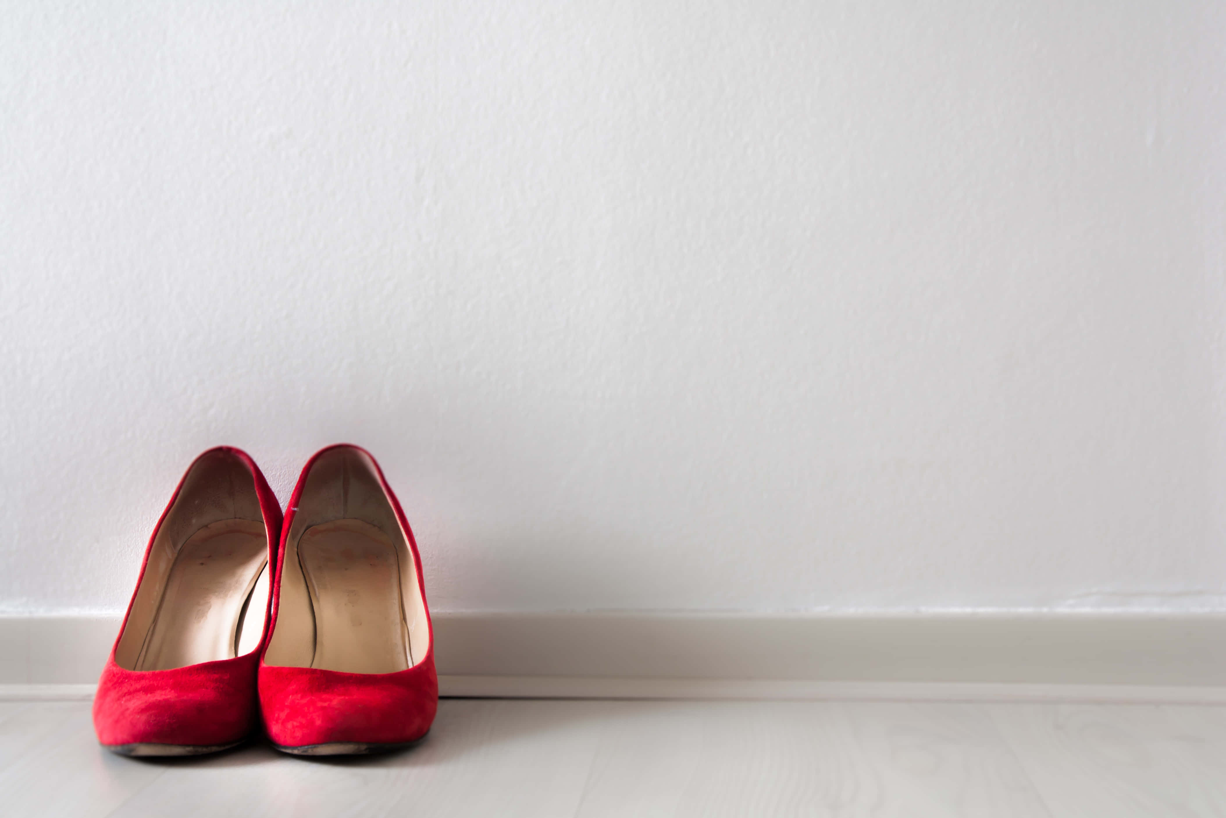 Footwear Design 桌布 壁紙 — 一對鮮紅色天鵝絨高跟鞋整齊地放在淺色木地板上，背景是純白牆壁。