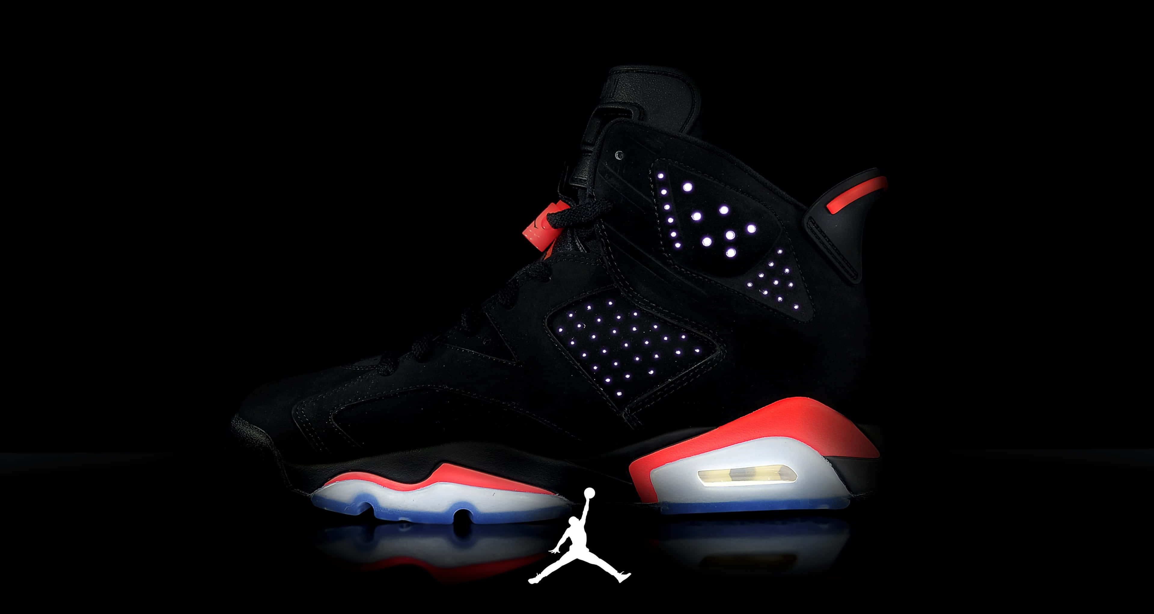 Air Jordan 4 Retro Infrared 壁紙 — 一對黑色Jordan 6運動鞋，帶有發光的白色圓點和紅色點綴，站在深色背景前，下方有反光表面和白色Jumpman標誌。