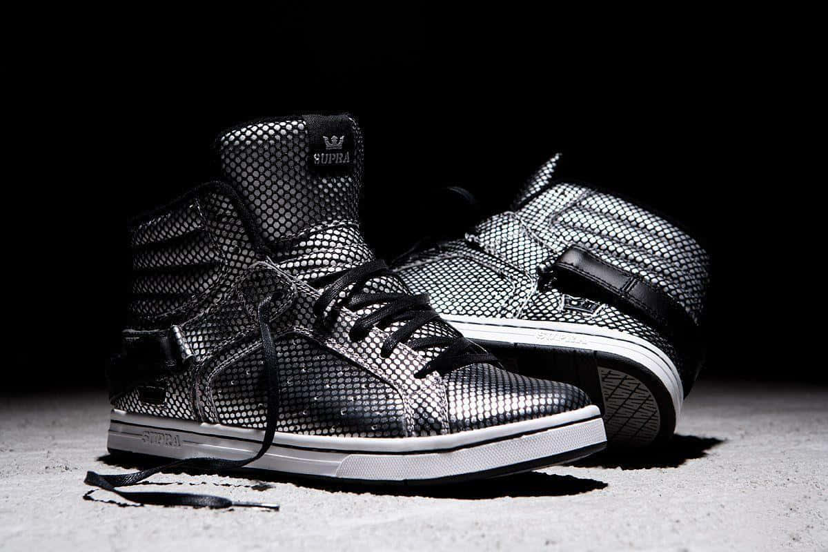 Footwear Design 桌布 壁紙 — 一對黑色網面高筒Supra運動鞋，搭配白色鞋底和黑色鞋帶，在混凝土表面上以黑暗背景戲劇性地打光。